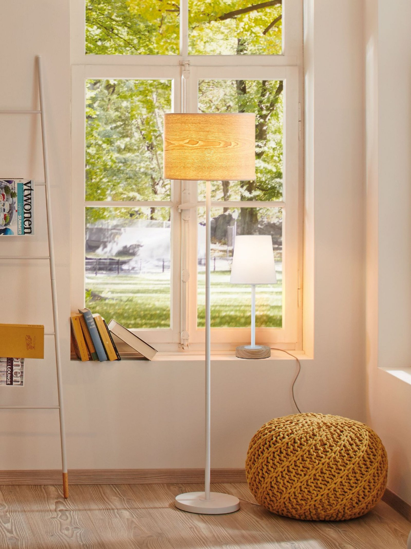 Ein Raum mit einer Stehlampe und einer Seitenlampe. Hinter den Lampen befindet sich ein Fenster und auf dem Boden ein Hocker.