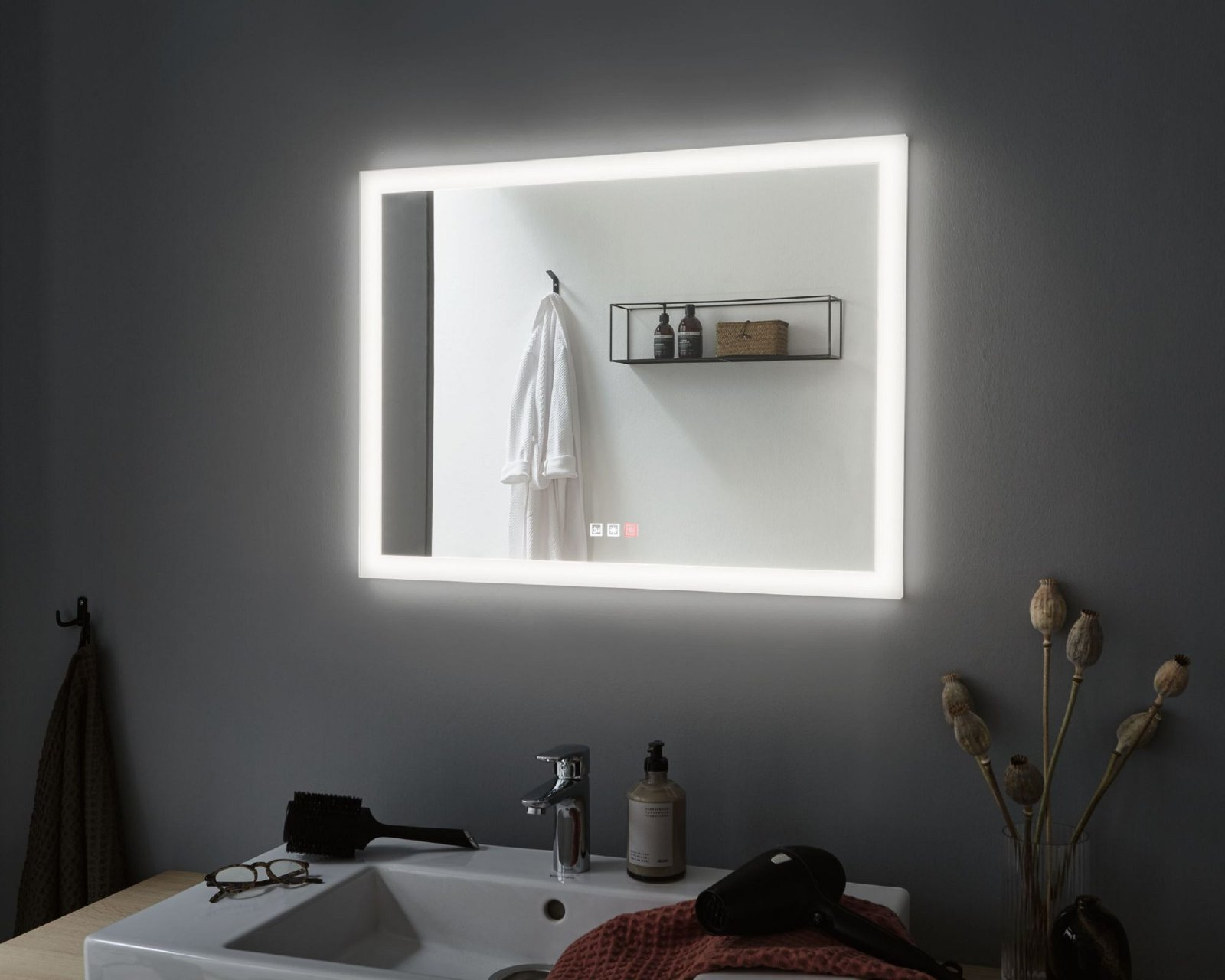 Miroir éclairé dans la salle de bain, avec serviette, étagère et lavabo.