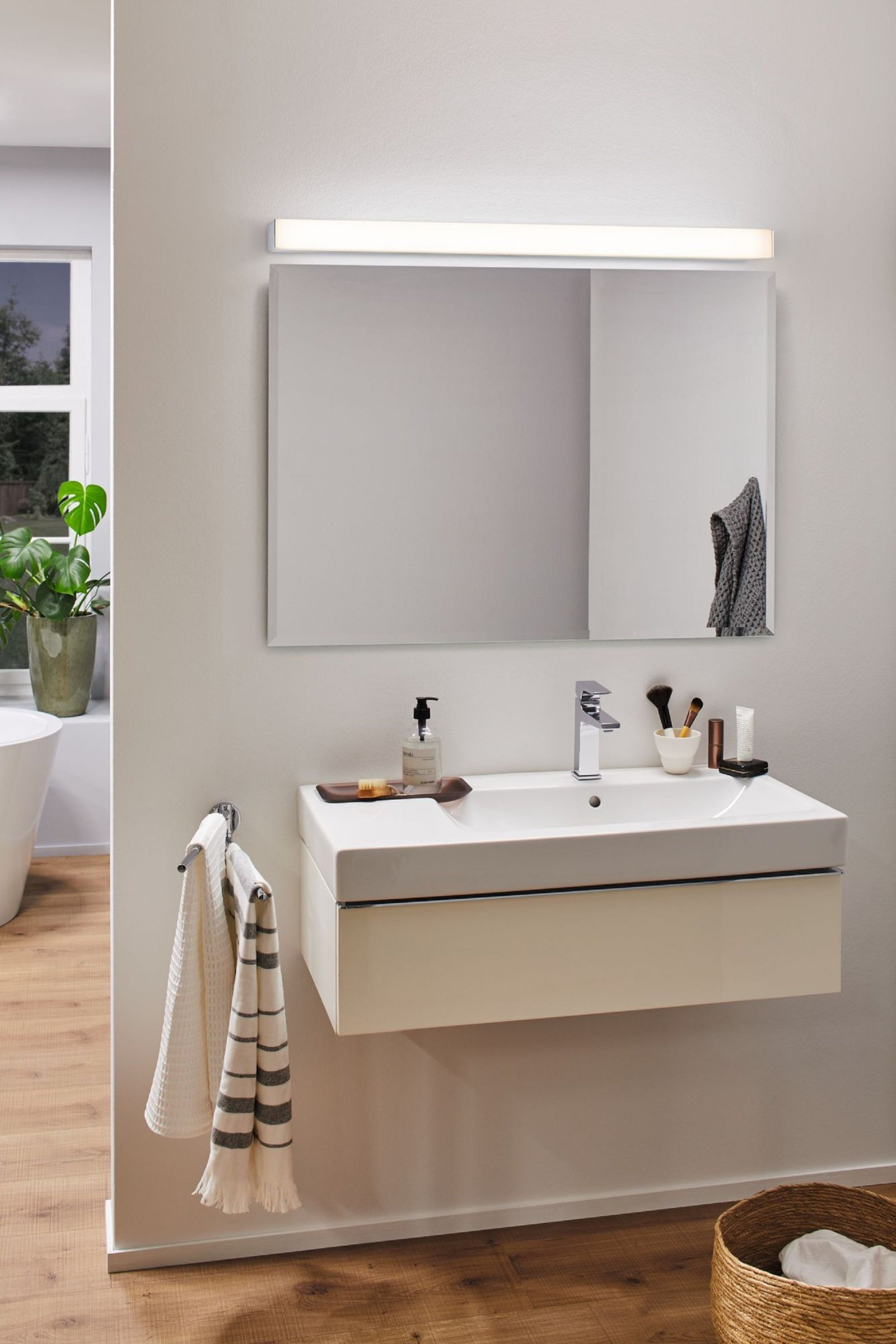 Badezimmer mit Spiegel über einem Waschbecken. Es gibt ein Handtuch und Toilettenartikel.