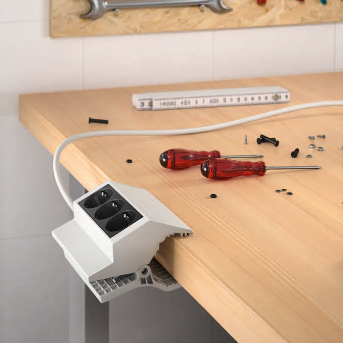 Warsztat z narzędziami i białą listwą zasilającą przymocowaną do boku. Obecne są śruby i miarka.