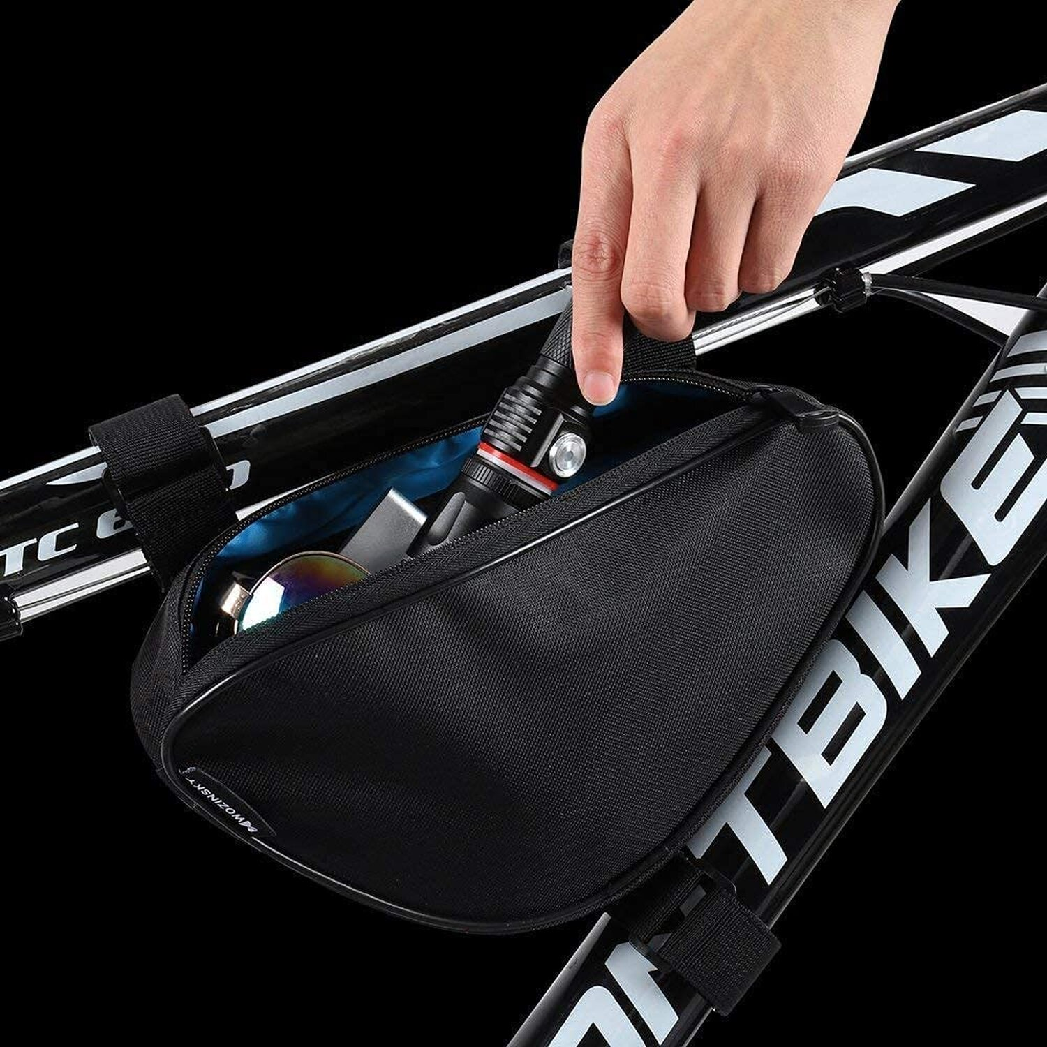 Eine Hand greift in eine schwarze Fahrradtasche am Fahrradrahmen.