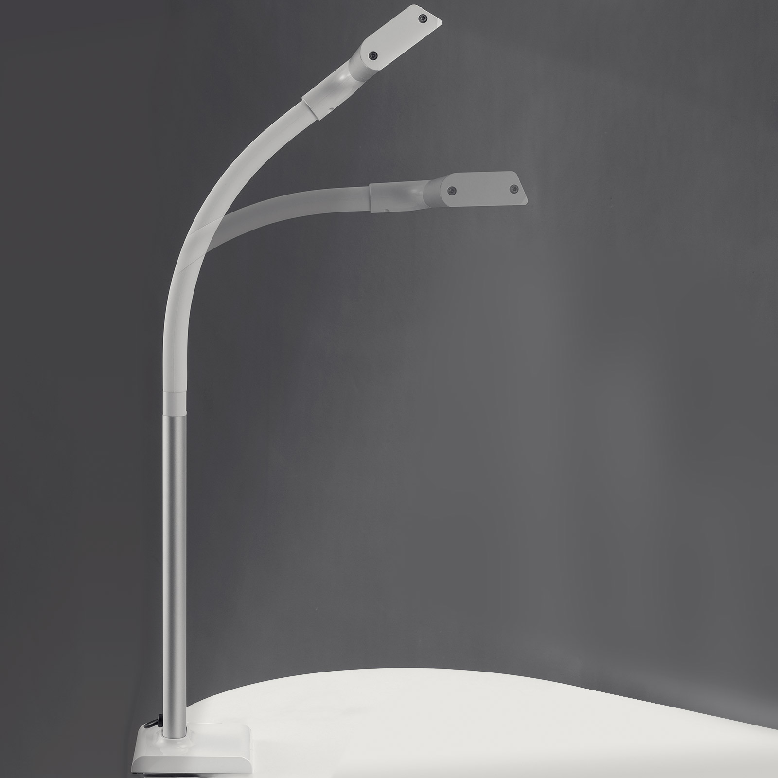 Lampada moderna bianca e argento, design curvo, su superficie bianca e sfondo grigio.