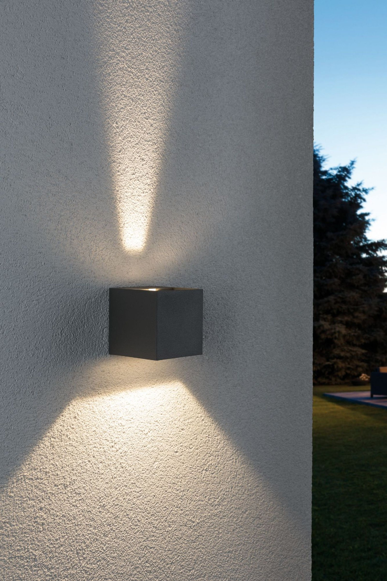 Kwadratowa oprawa oświetleniowa zewnętrzna zamontowana na teksturowanej ścianie. Promienie światła w górę i w dół.