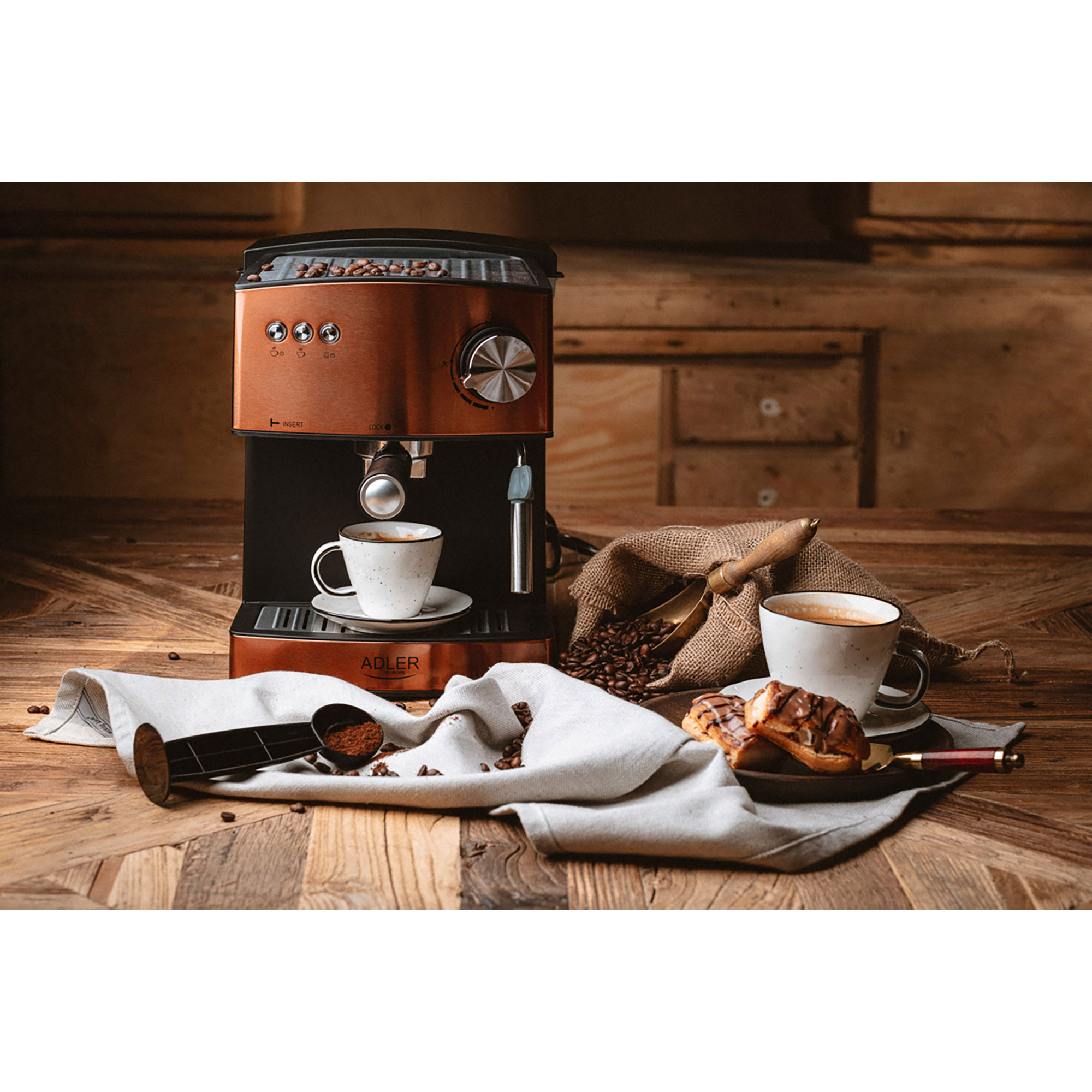 Una macchina per caffè espresso in rame con tazze di caffè, chicchi e pasticcini, su un tavolo di legno.
