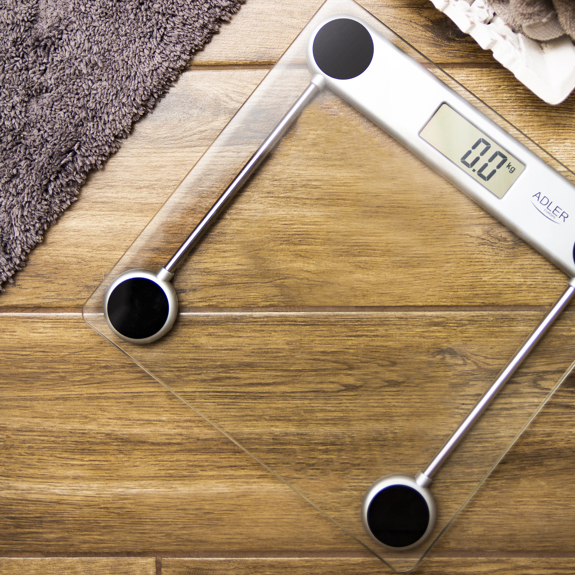 Digitale Waage mit Handtuch und Holzboden. Die Waage zeigt 0,0 kg an.
