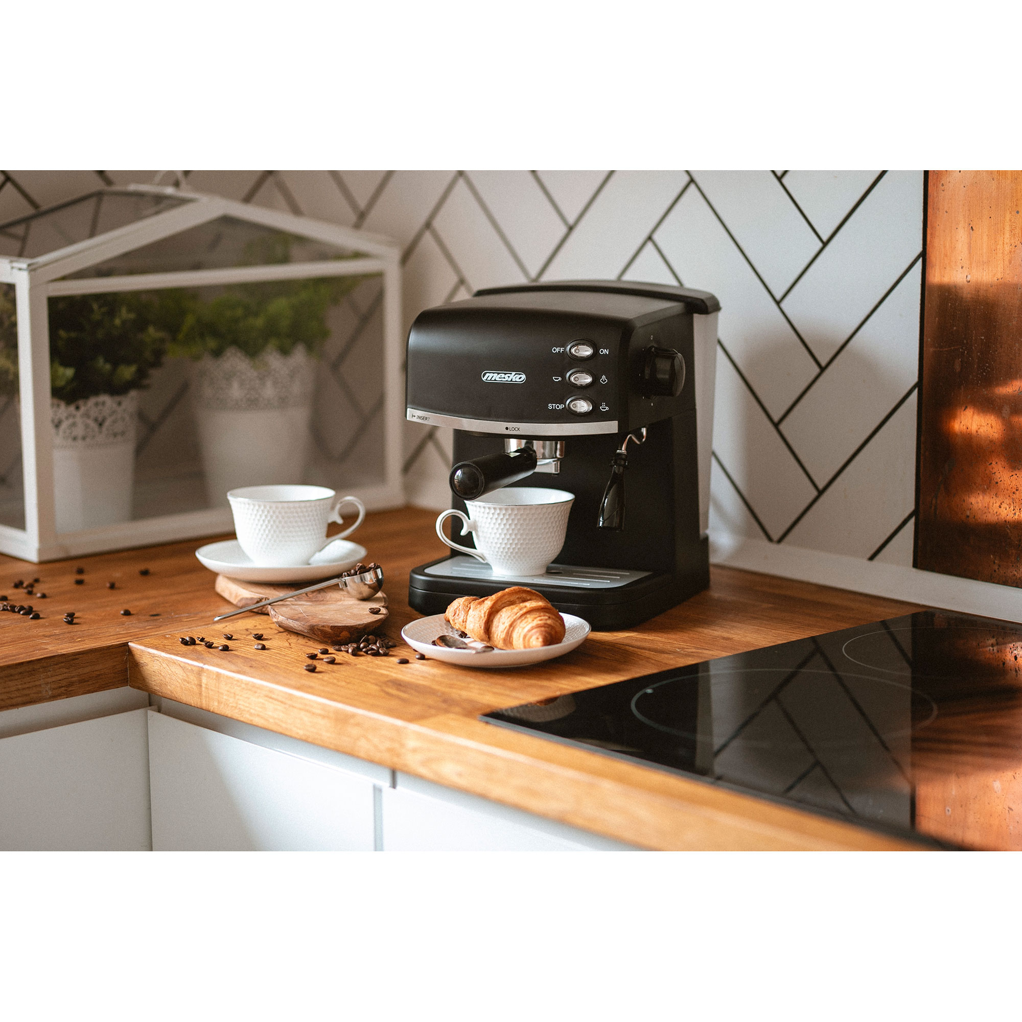 Ekspres do kawy z filiżankami, rogalikami i ziarnami kawy na drewnianym blacie.