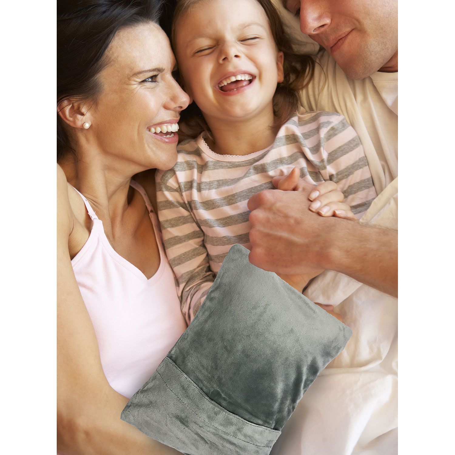 Familia en la cama, riendo, con una almohadilla térmica gris. El enfoque está en los rostros felices.