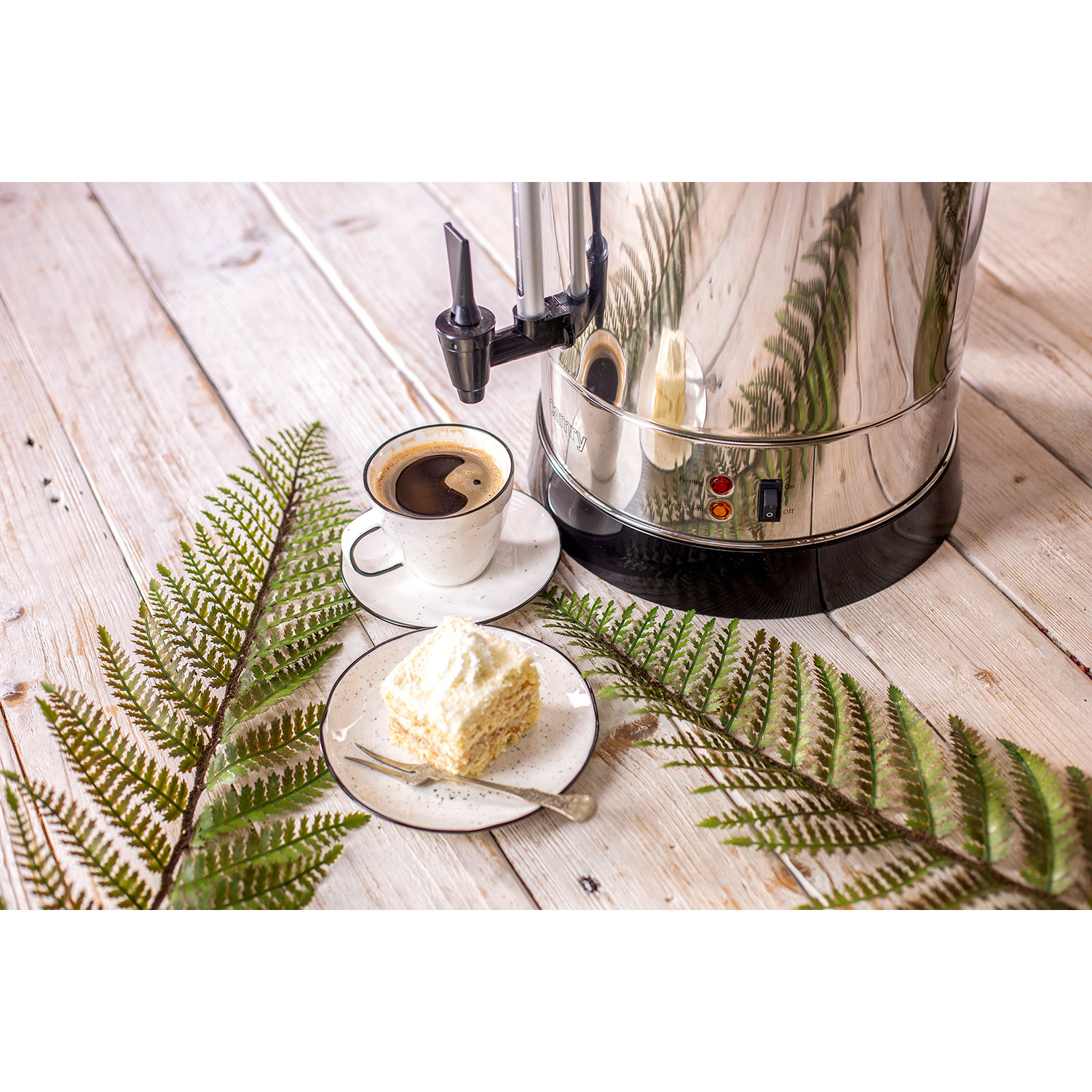 Ekspres do kawy z filiżanką kawy, ciastem i liśćmi paproci na drewnianym stole.