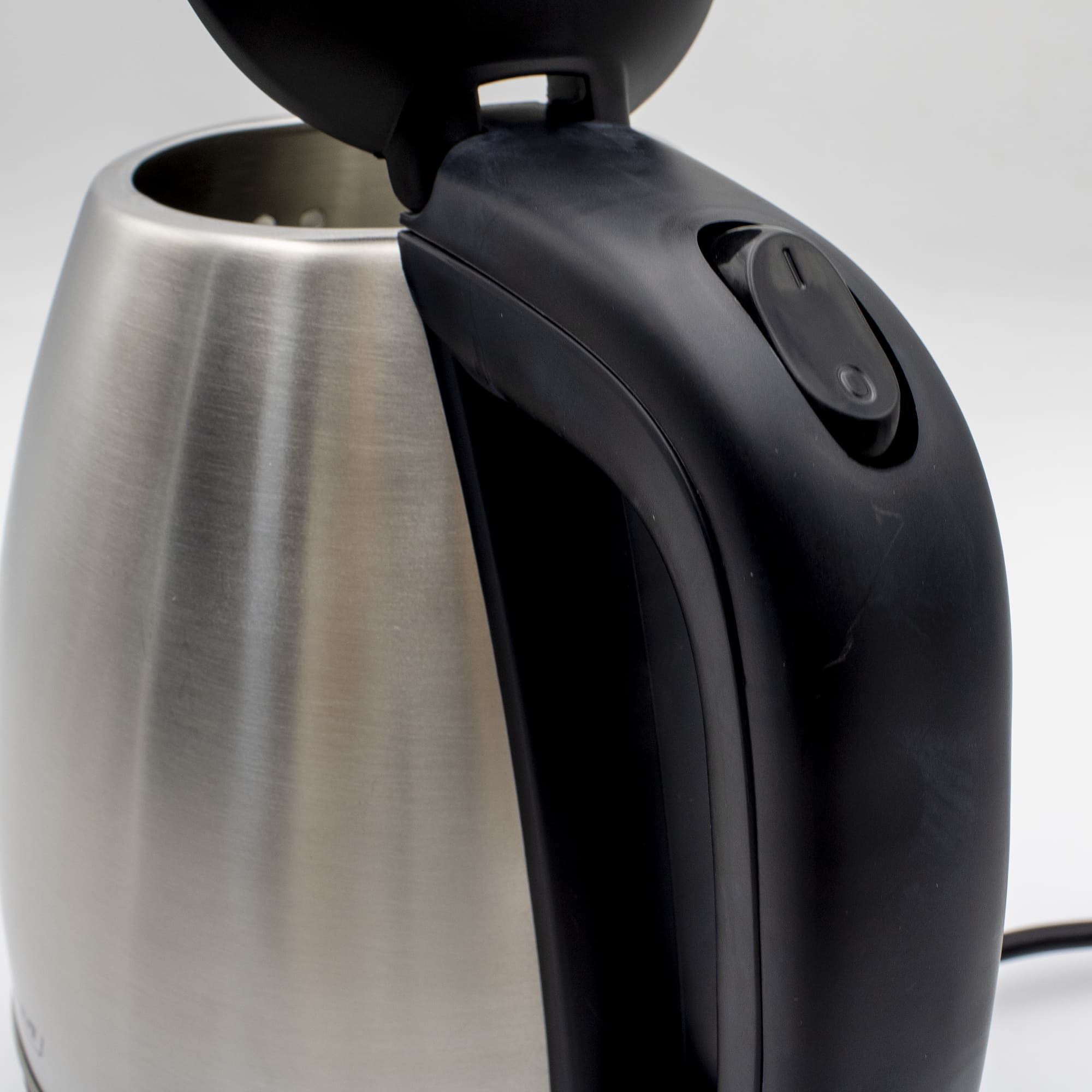 Zbliżenie srebrnego i czarnego czajnika elektrycznego z czarnym uchwytem, otwartą pokrywą.