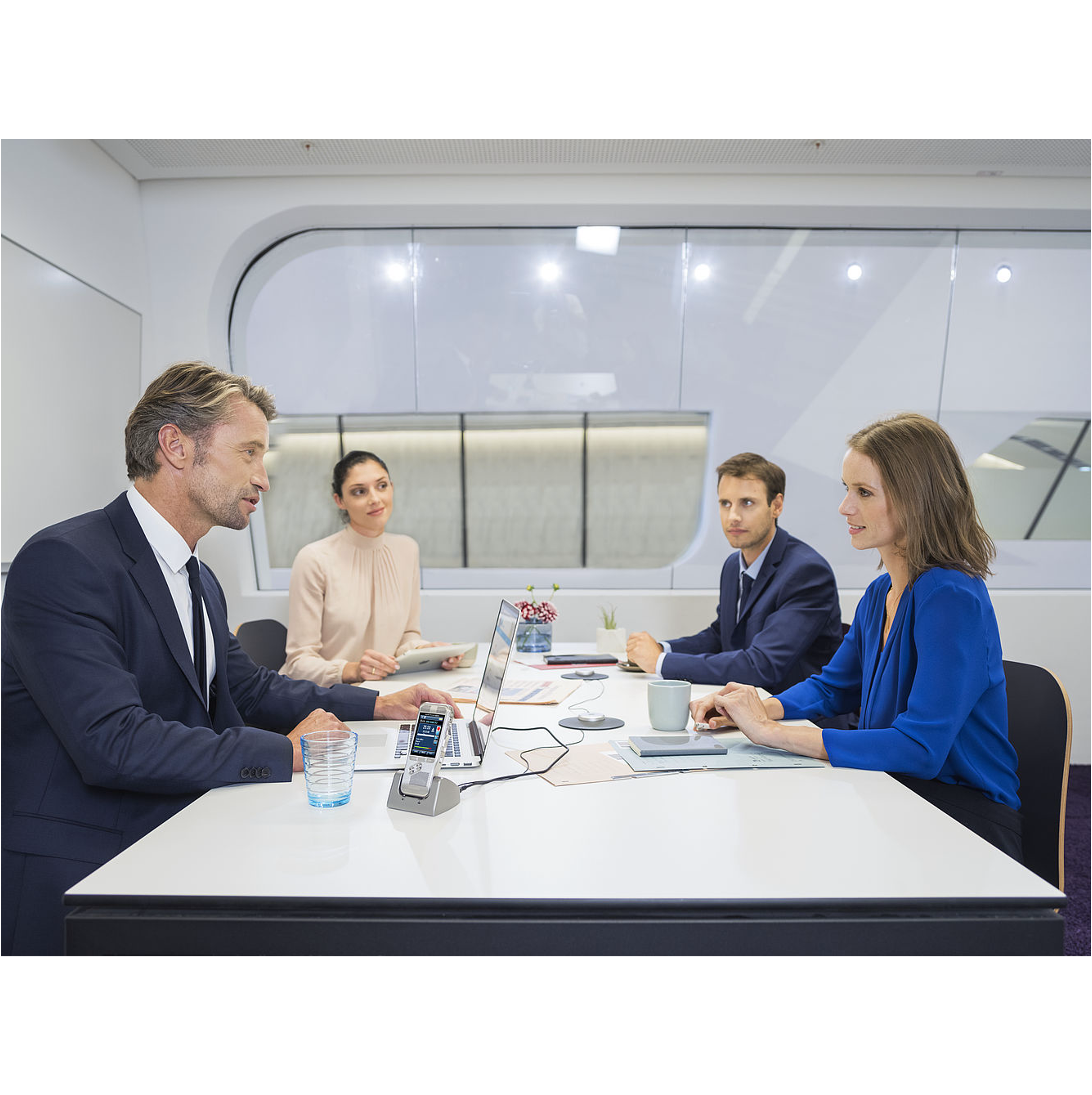 Vier Personen in einem Meeting, sitzen um einen Tisch mit Laptop und Telefon.