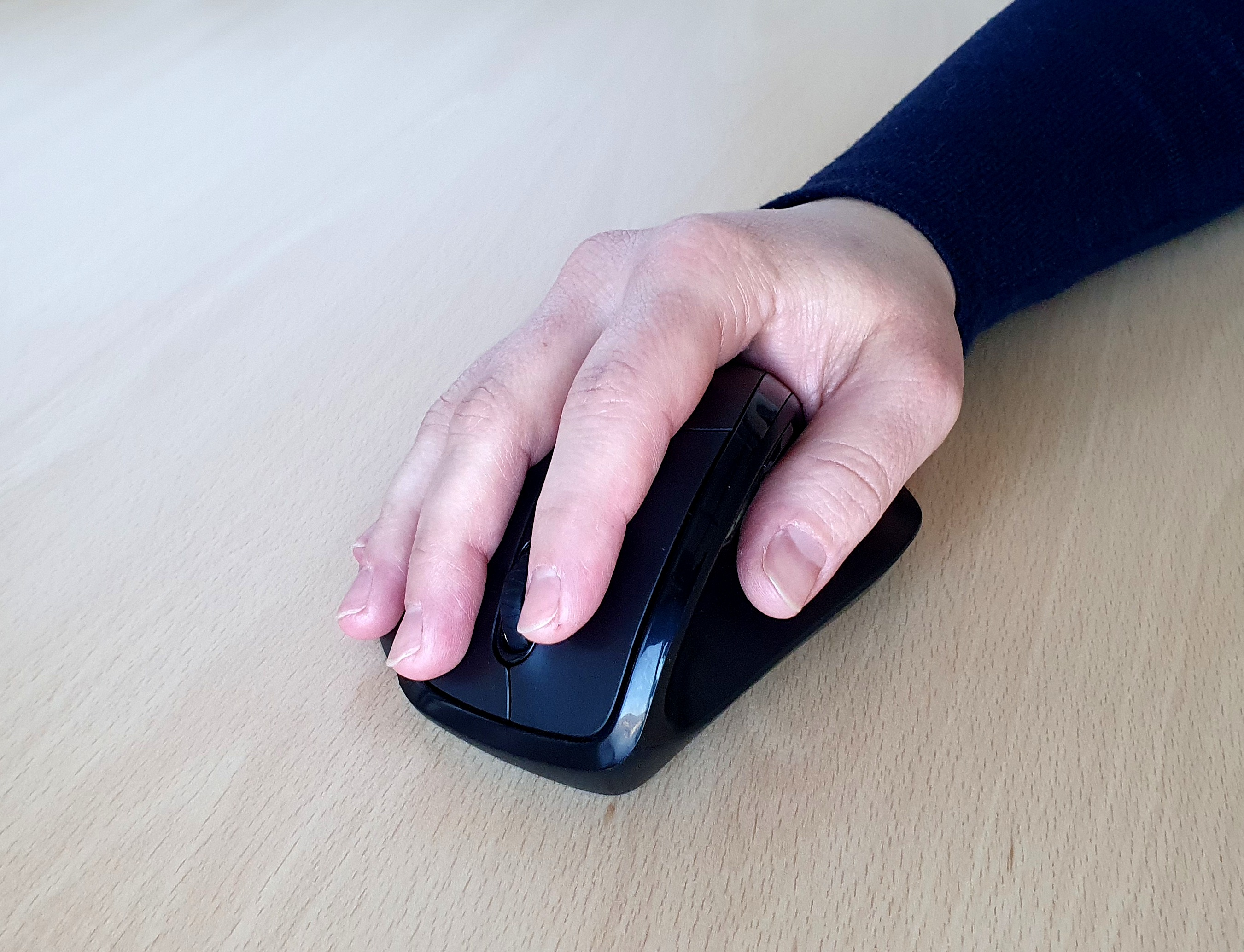 Eine Hand liegt auf einer schwarzen Computermaus auf einer Holzoberfläche.
