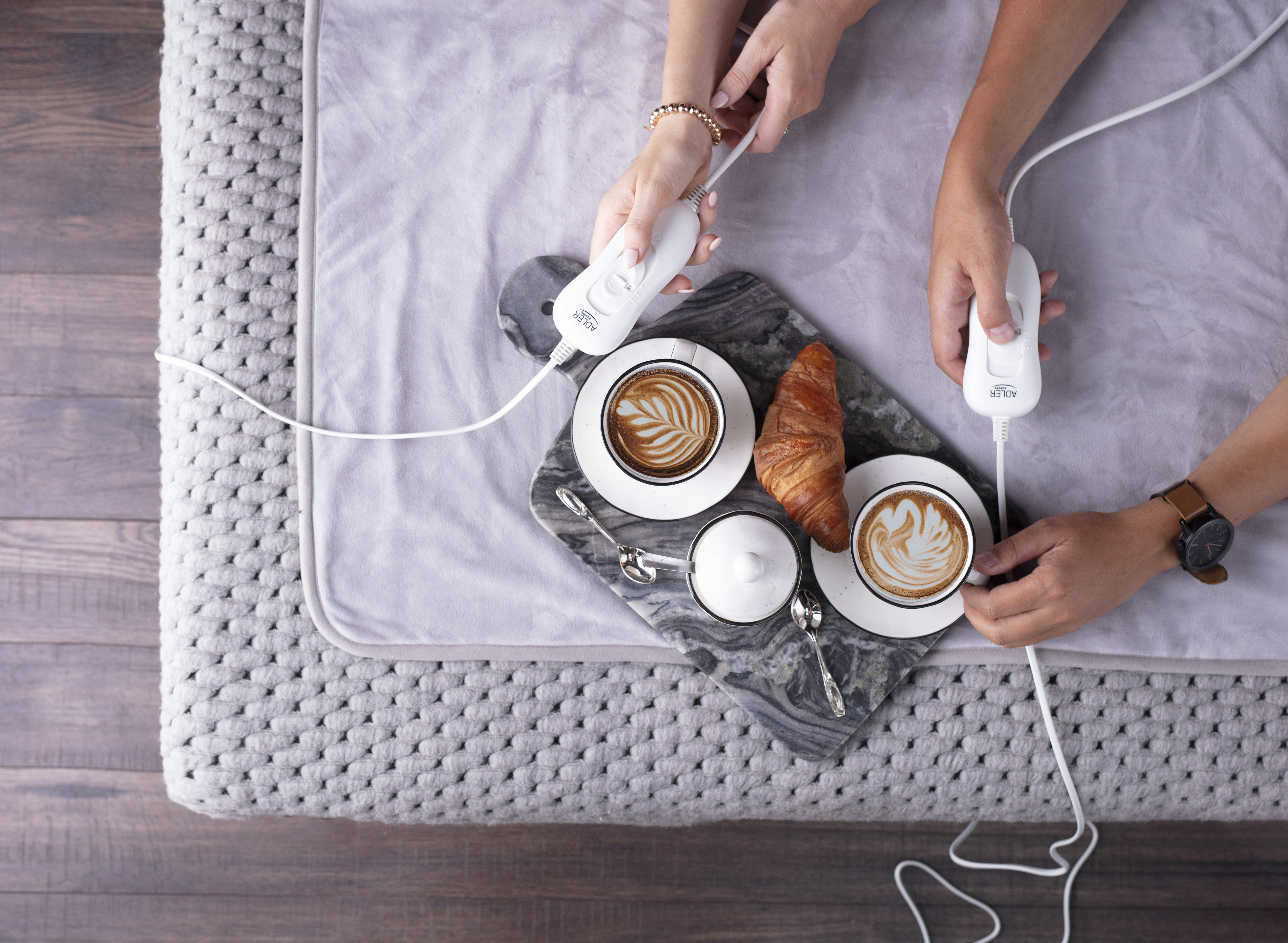 Ręce trzymające białe kontrolery nad szarym kocem z tacą kawy i rogalików.