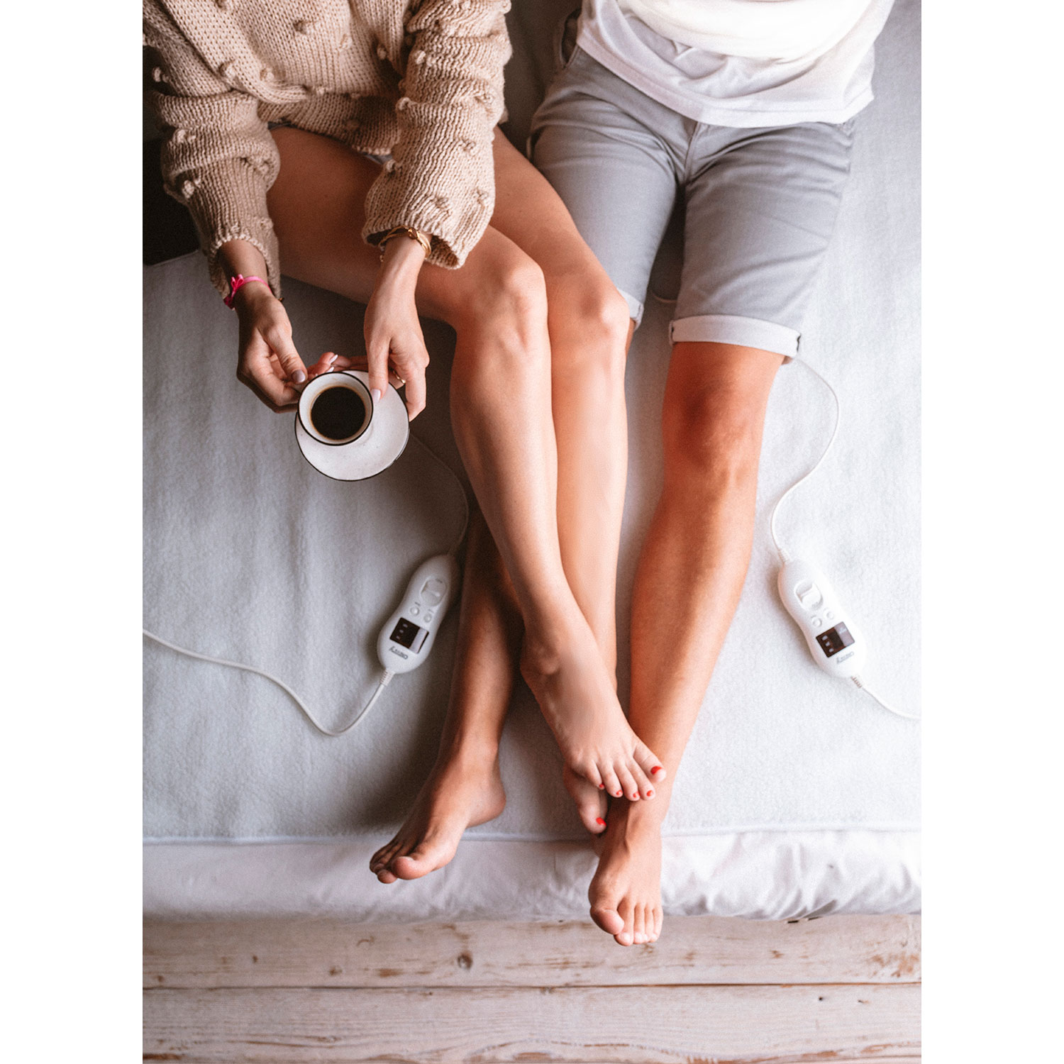 Top view of a couple in bed. Person holding a coffee cup and a person's legs with red nails.