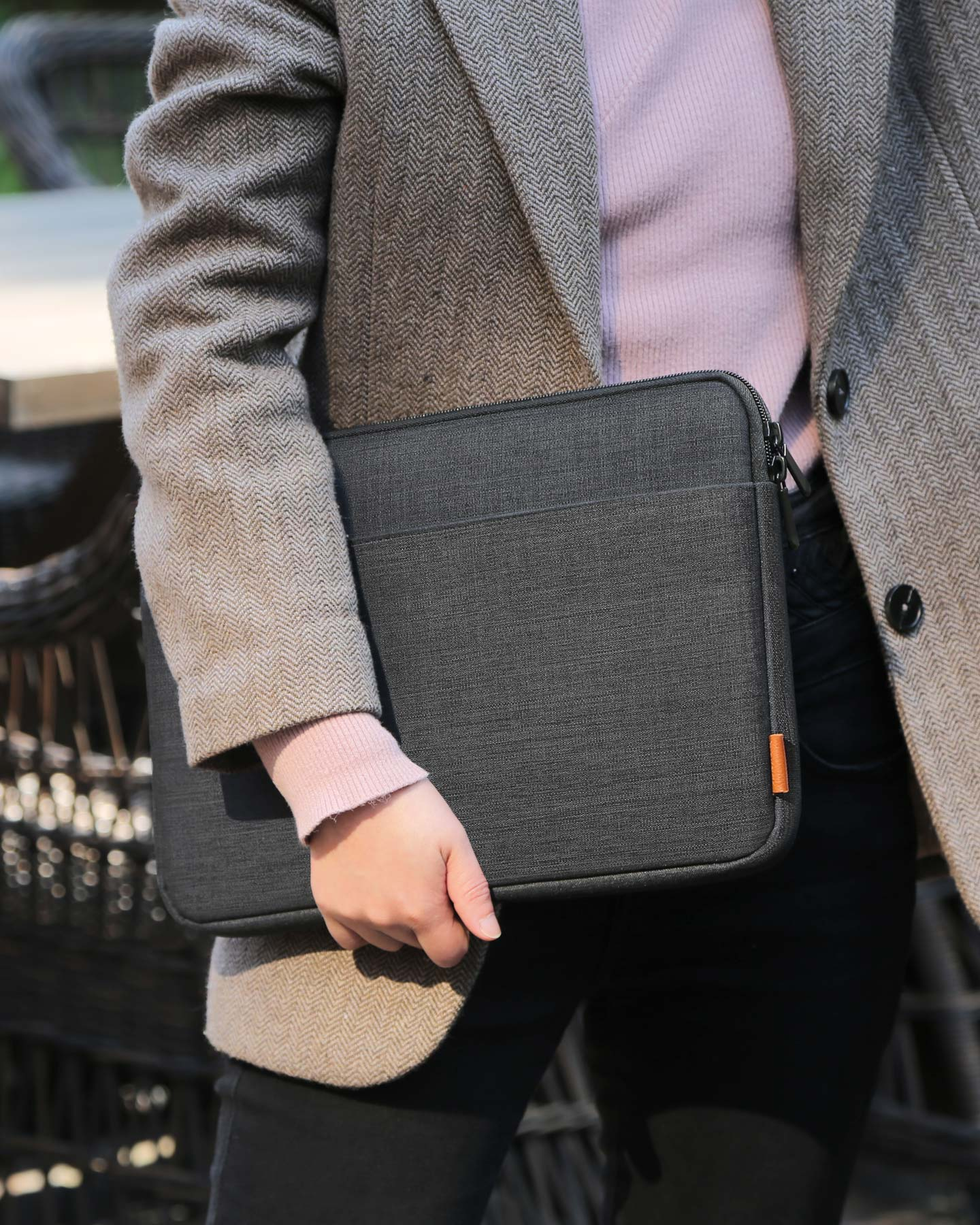 Eine Person hält eine dunkelgraue Laptoptasche. Sie trägt einen grauen Mantel und ein rosa Hemd.