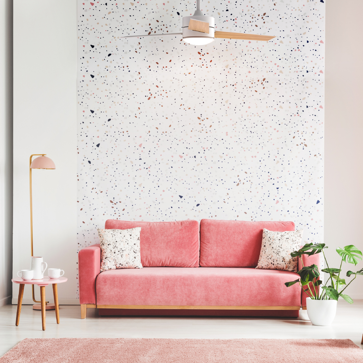 Divano, lampada e tappeto rosa in una stanza con parete a motivi e ventilatore a soffitto.
