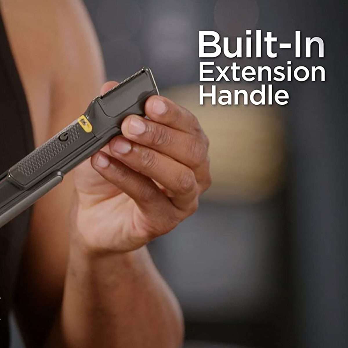 Mano de una persona sosteniendo una recortadora de cabello negra con un mango de extensión incorporado, y el texto 'Built-in Extension Handle'.