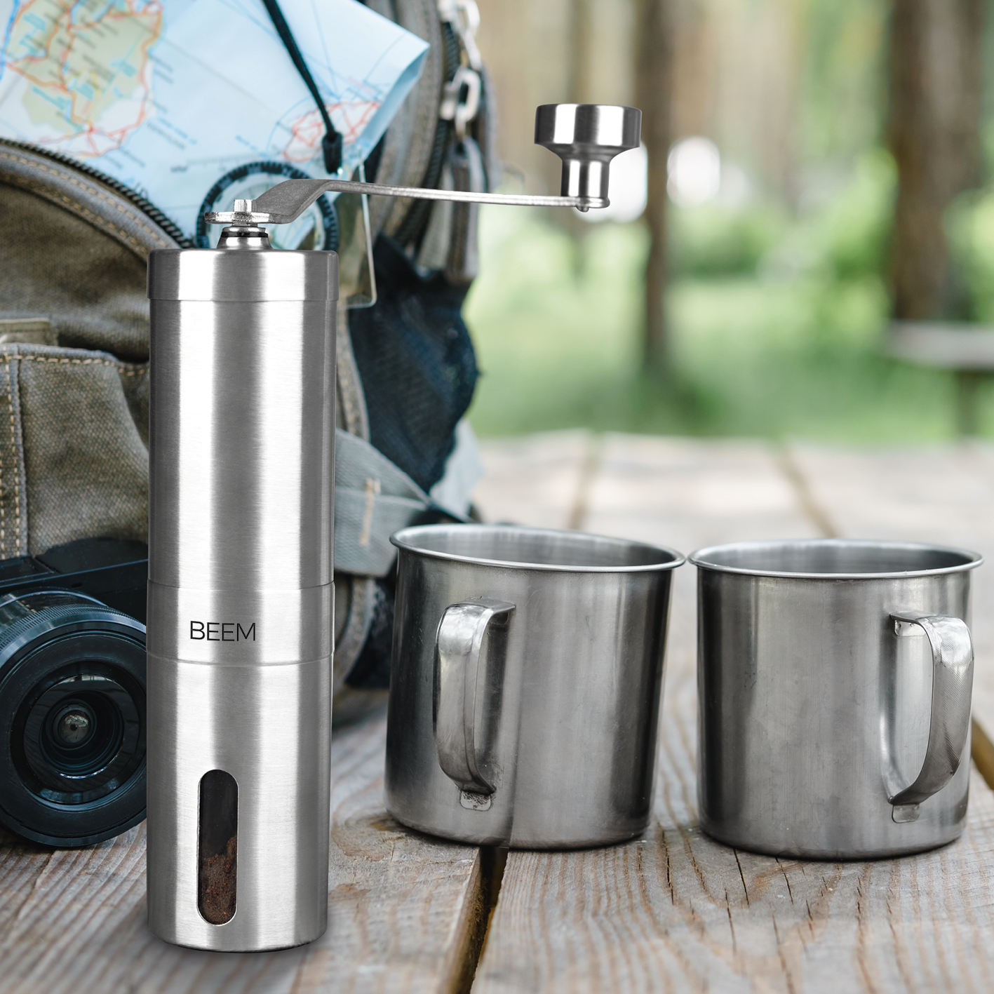 Silberne Kaffeemühle mit zwei Metallbechern und einer Karte im Hintergrund.