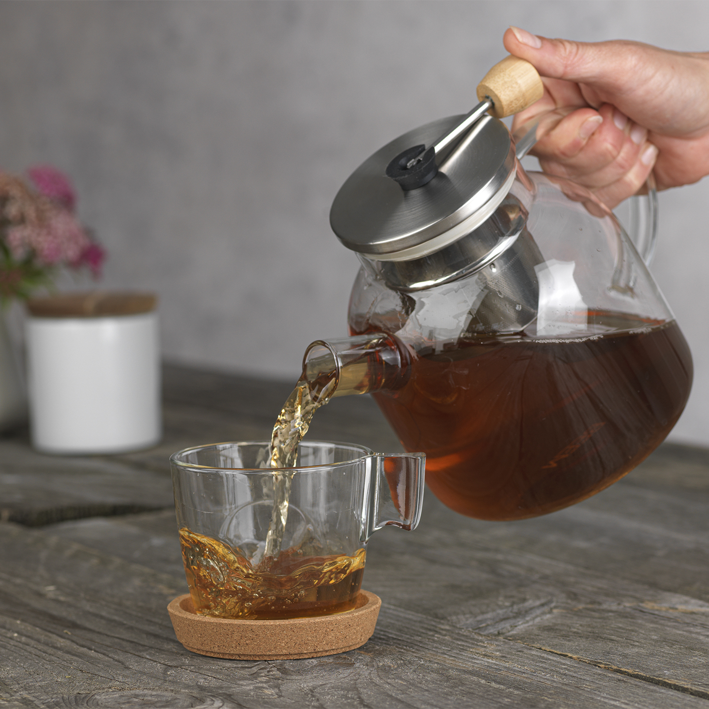Tee wird aus einer Glas-Teekanne in eine Tasse auf einem Untersetzer gegossen.