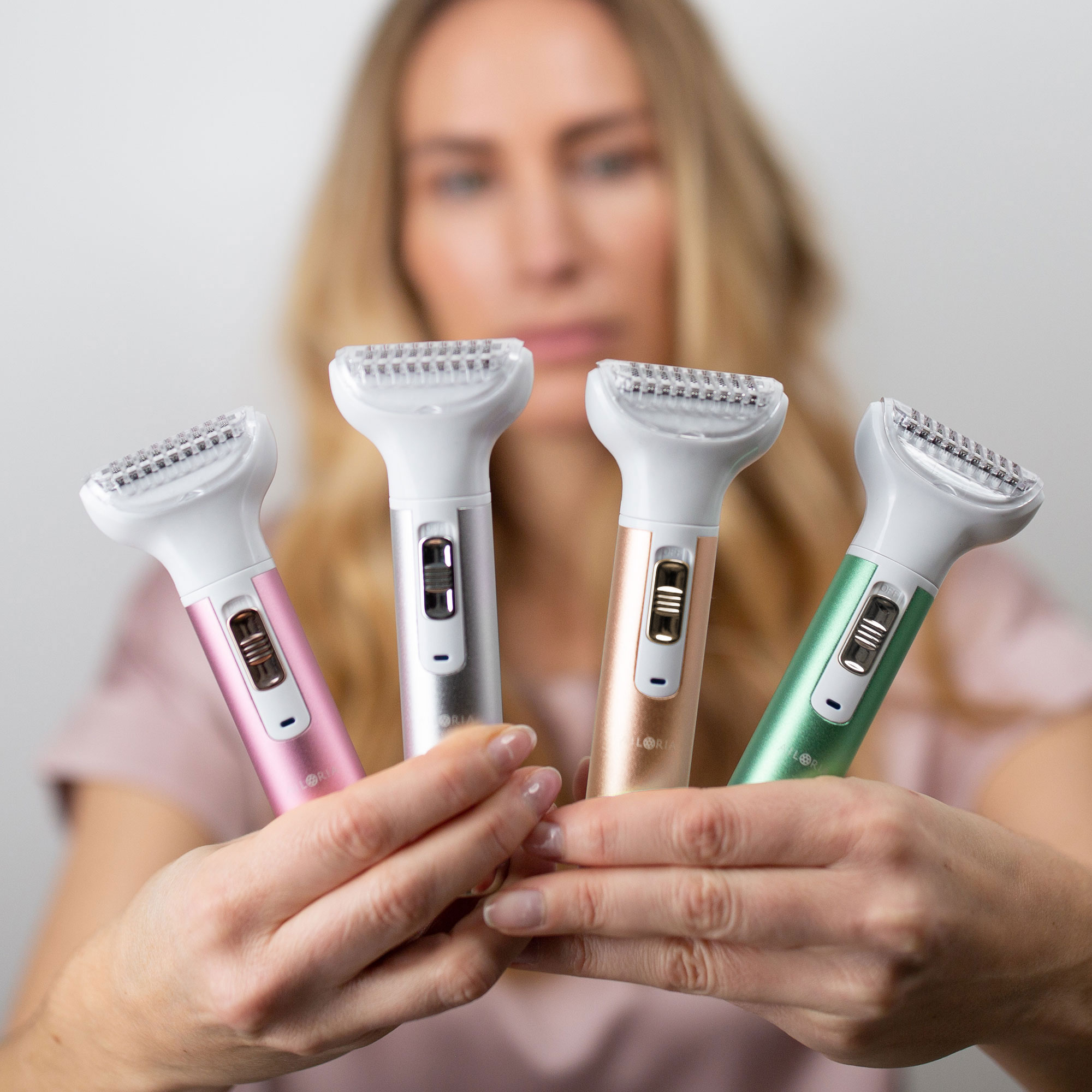 Frau hält vier elektrische Rasierer in Pink, Silber, Bronze und Grün.