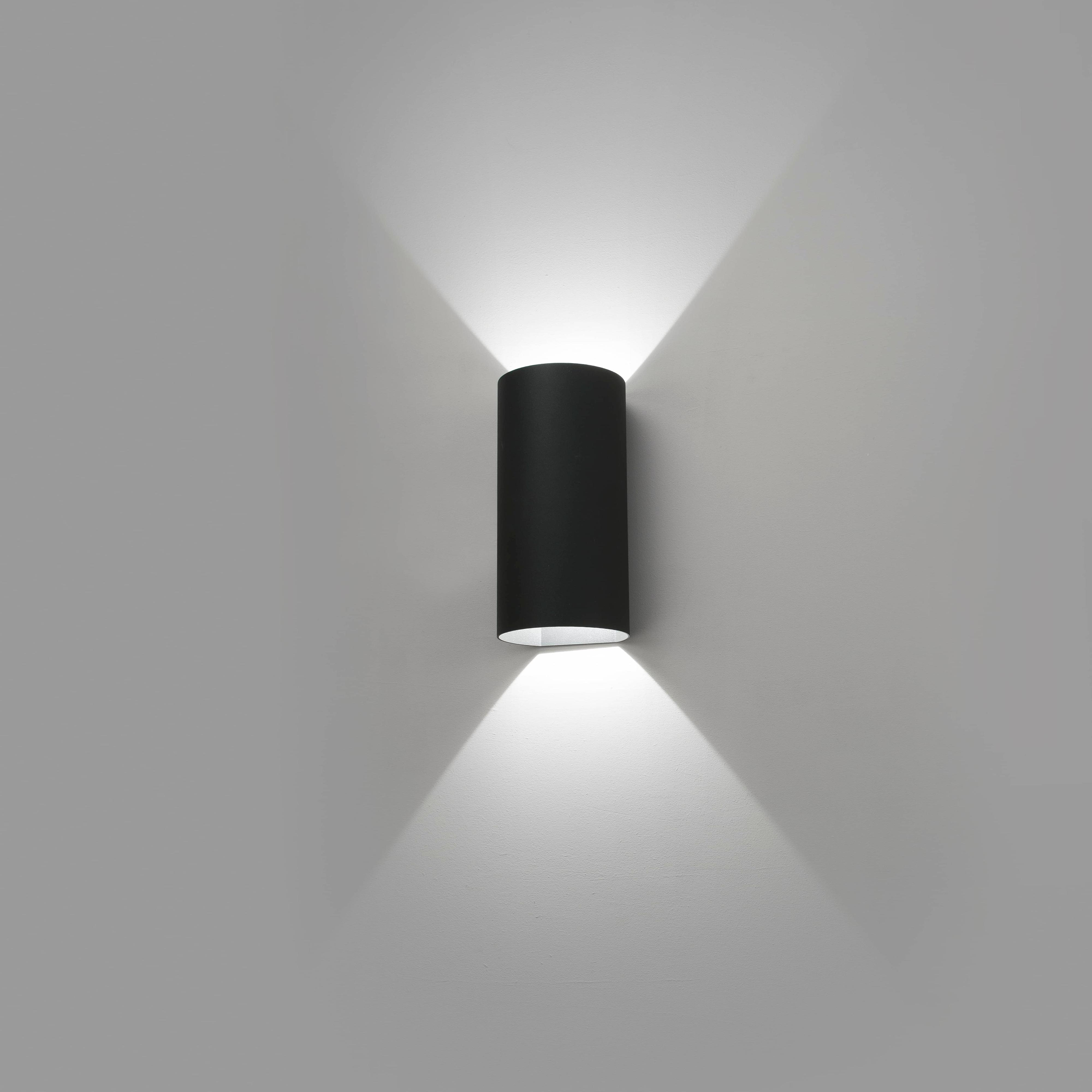 Schwarze zylindrische Wandleuchte, die Licht nach oben und unten wirft. Licht an einer weißen Wand.