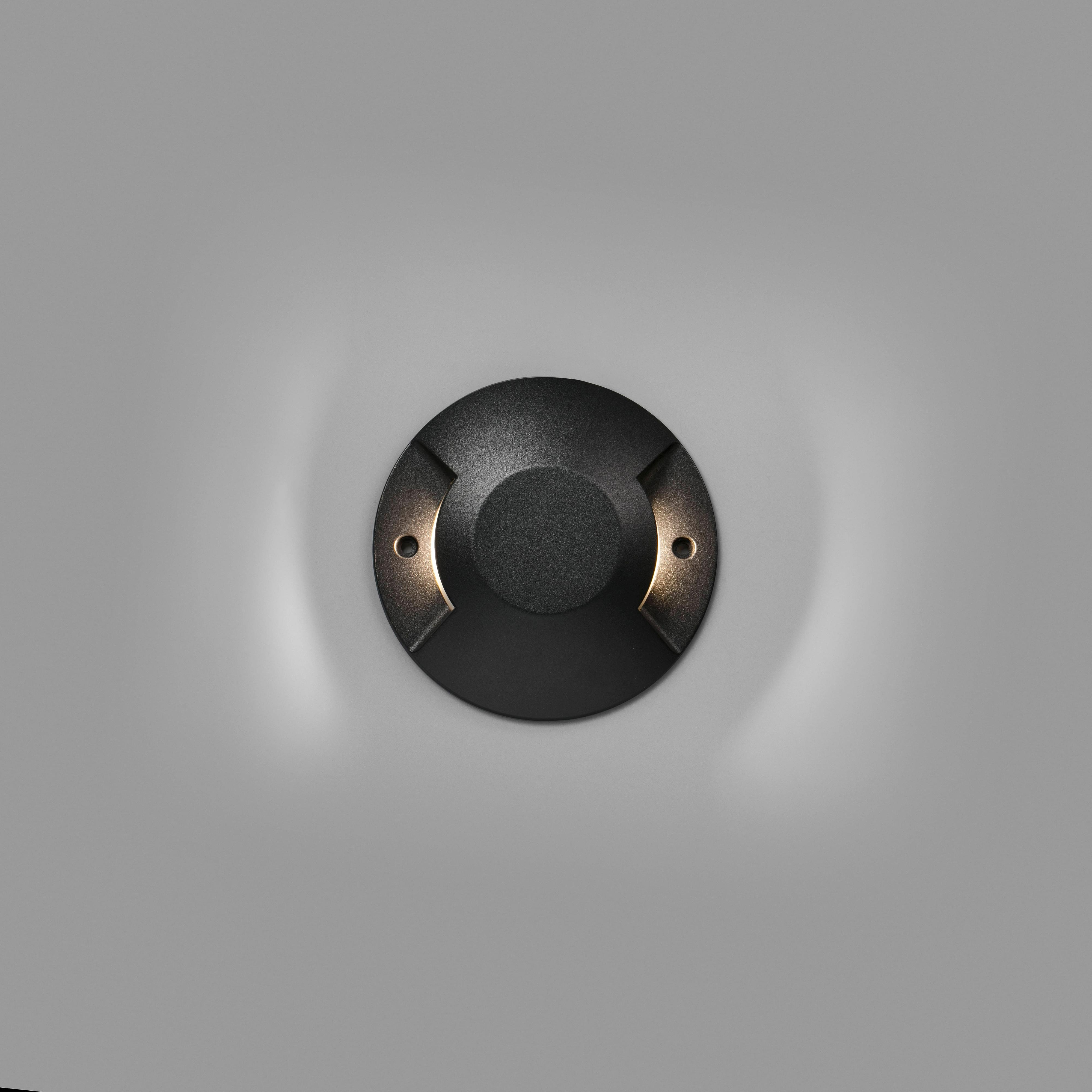 Un apparecchio di illuminazione rotondo nero per esterni su un muro grigio. Ha due sorgenti luminose.