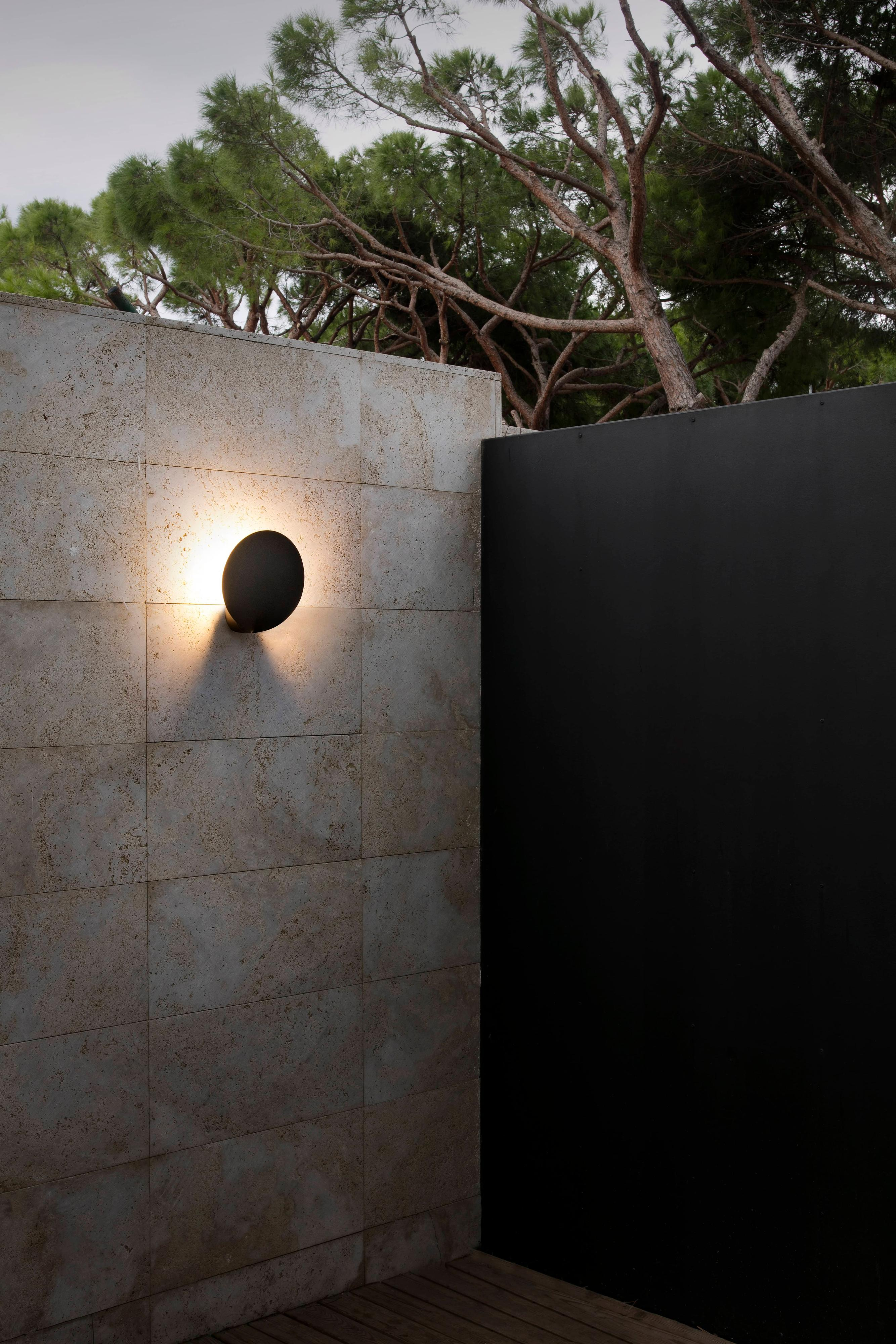 Muro esterno con lampada ovale e pannello nero.