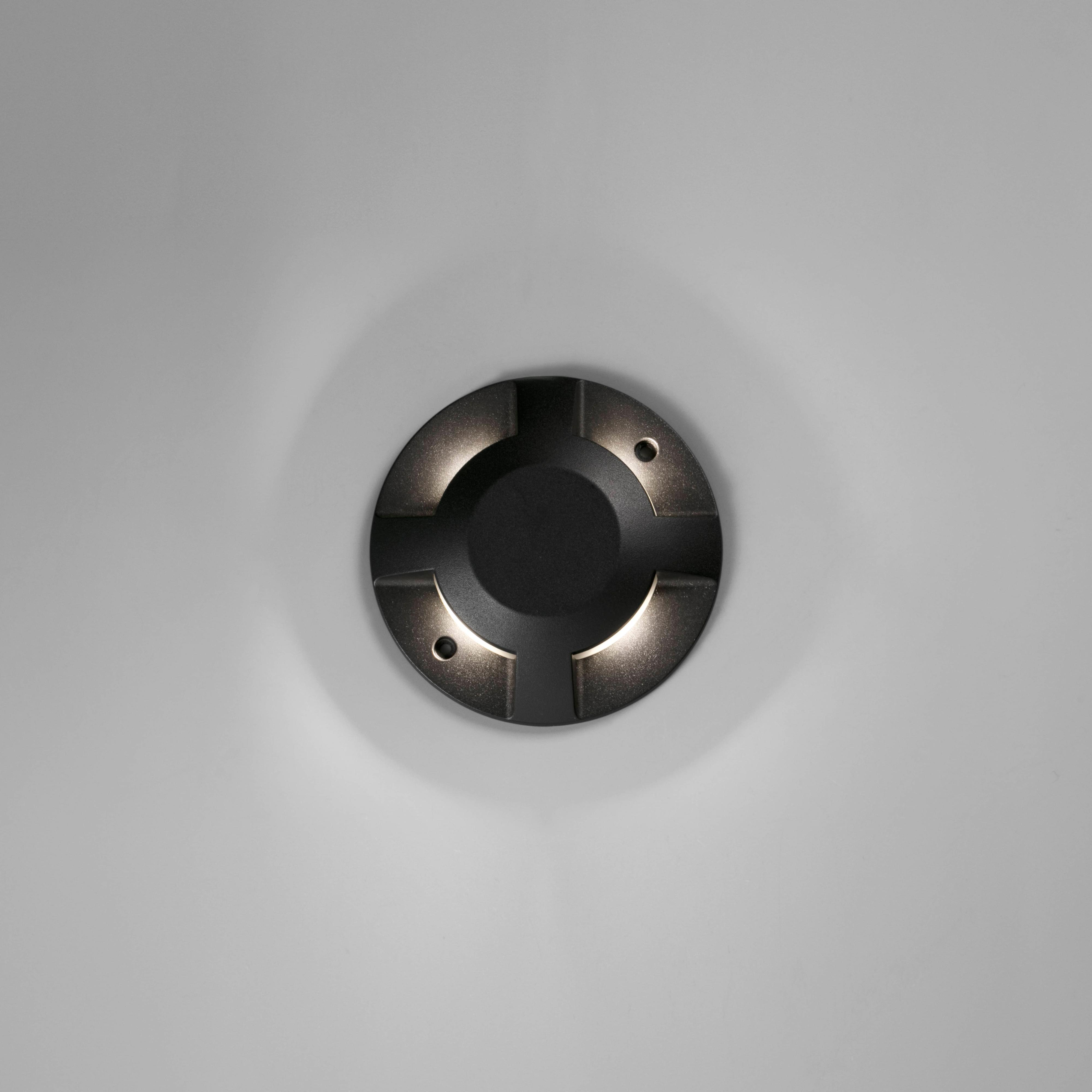 Un apparecchio di illuminazione circolare nero è montato su una superficie grigio chiaro, con tre piccole luci.