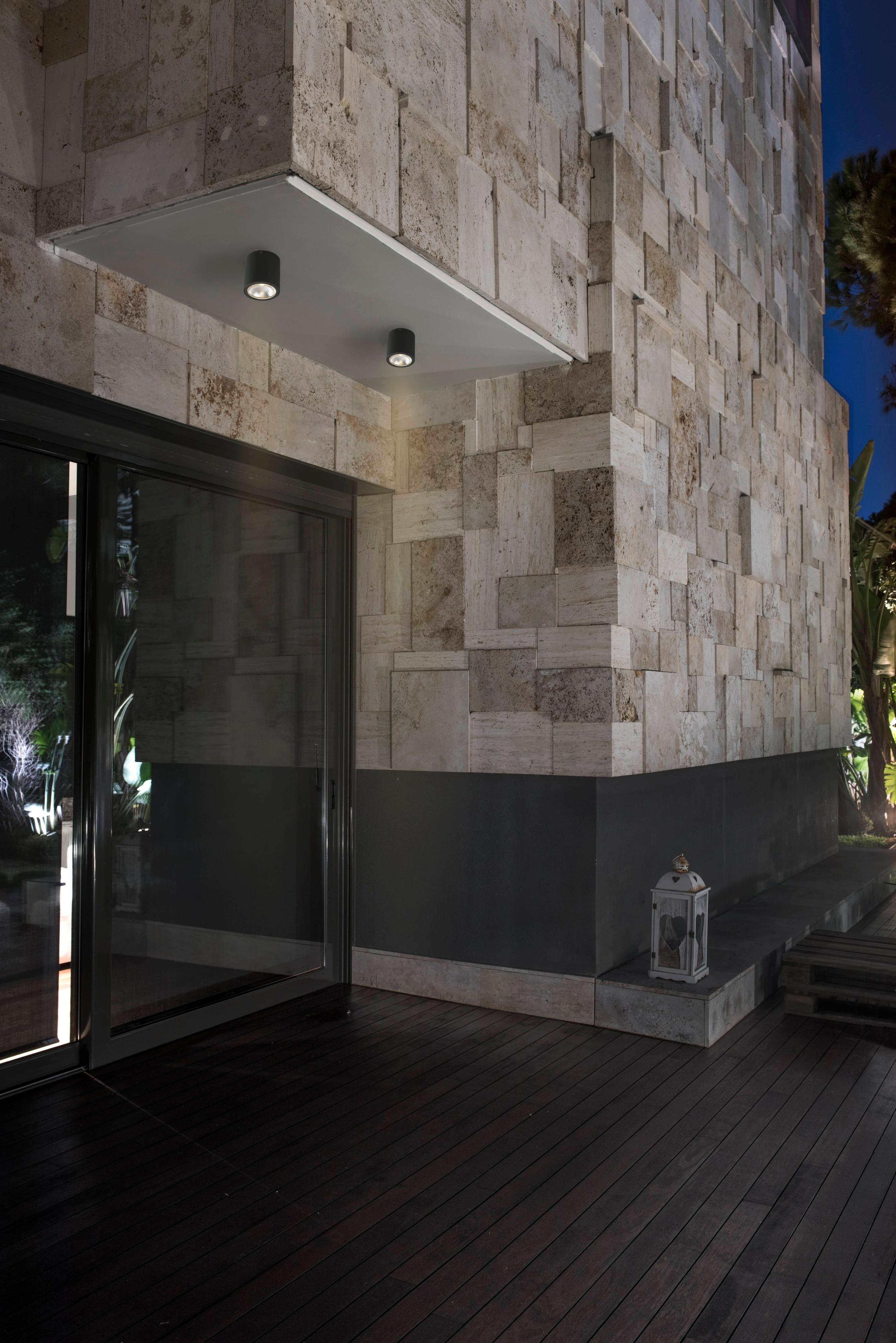 Esterno di un edificio con muri in pietra, terrazza in legno scuro, porta a vetri e una piccola lanterna.