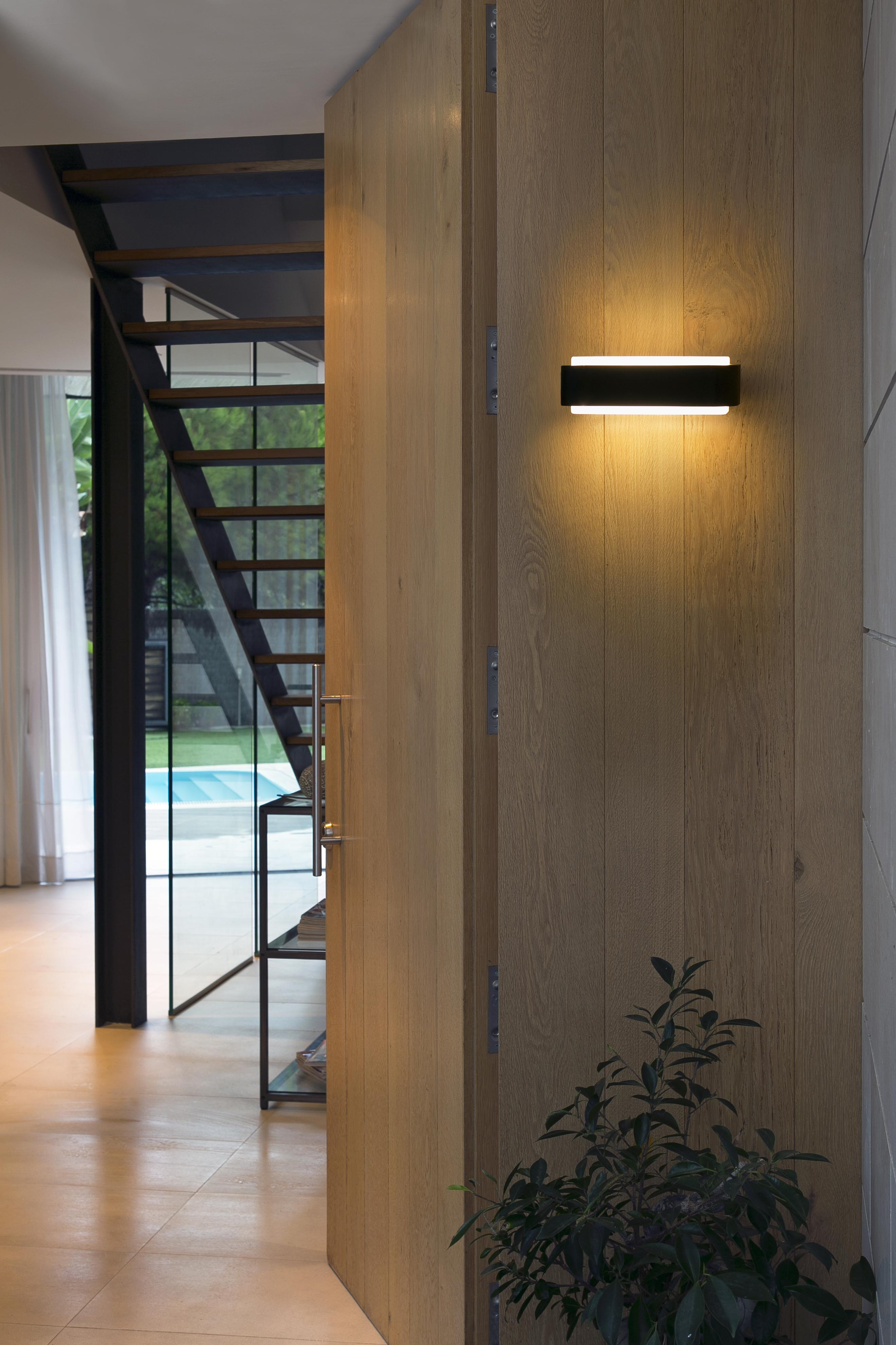 Un apparecchio di illuminazione a parete, con una porta in legno e scale dietro. La scena è ben illuminata.