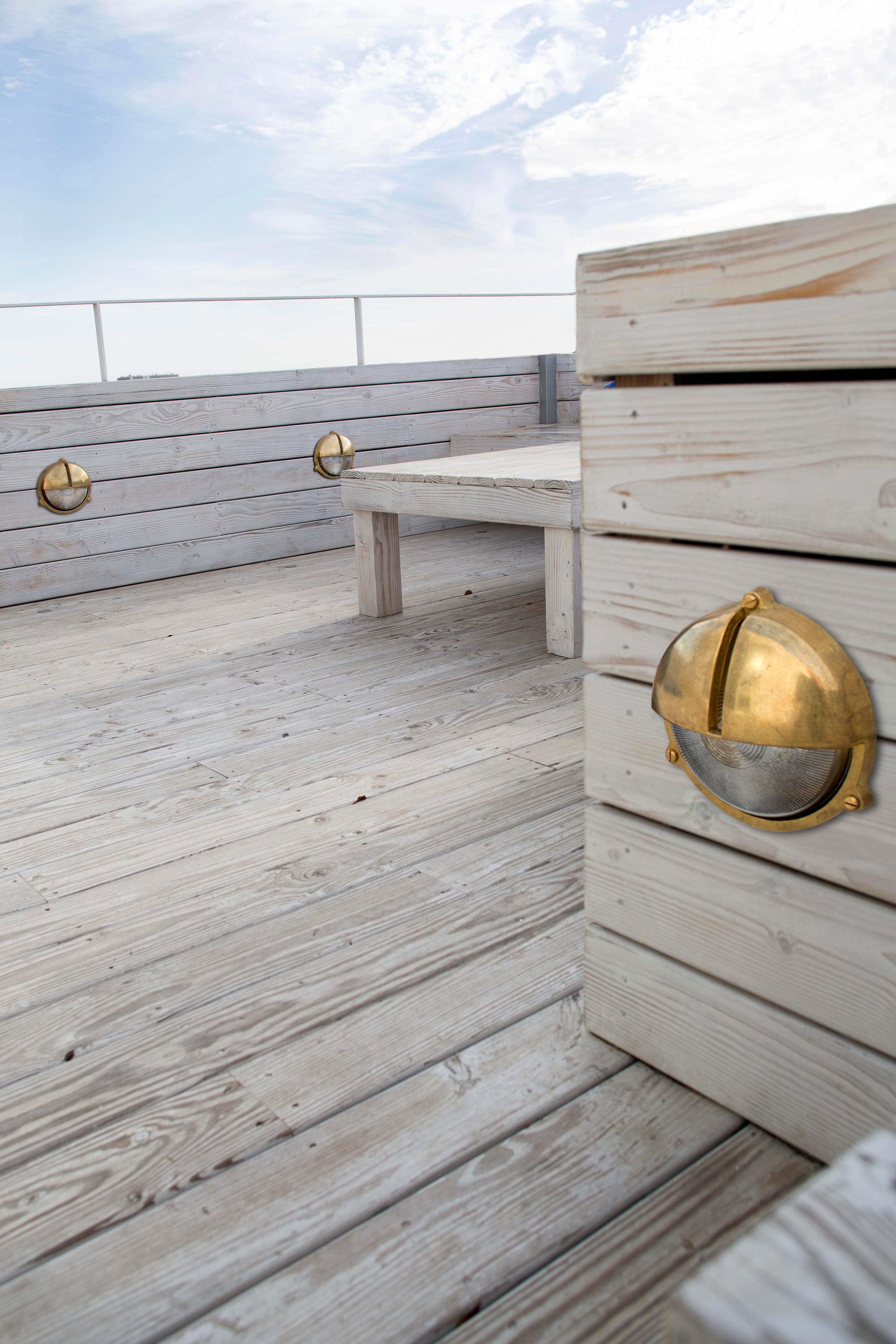 Un ponte di legno chiaro con luci a parete color oro e un cielo azzurro chiaro.