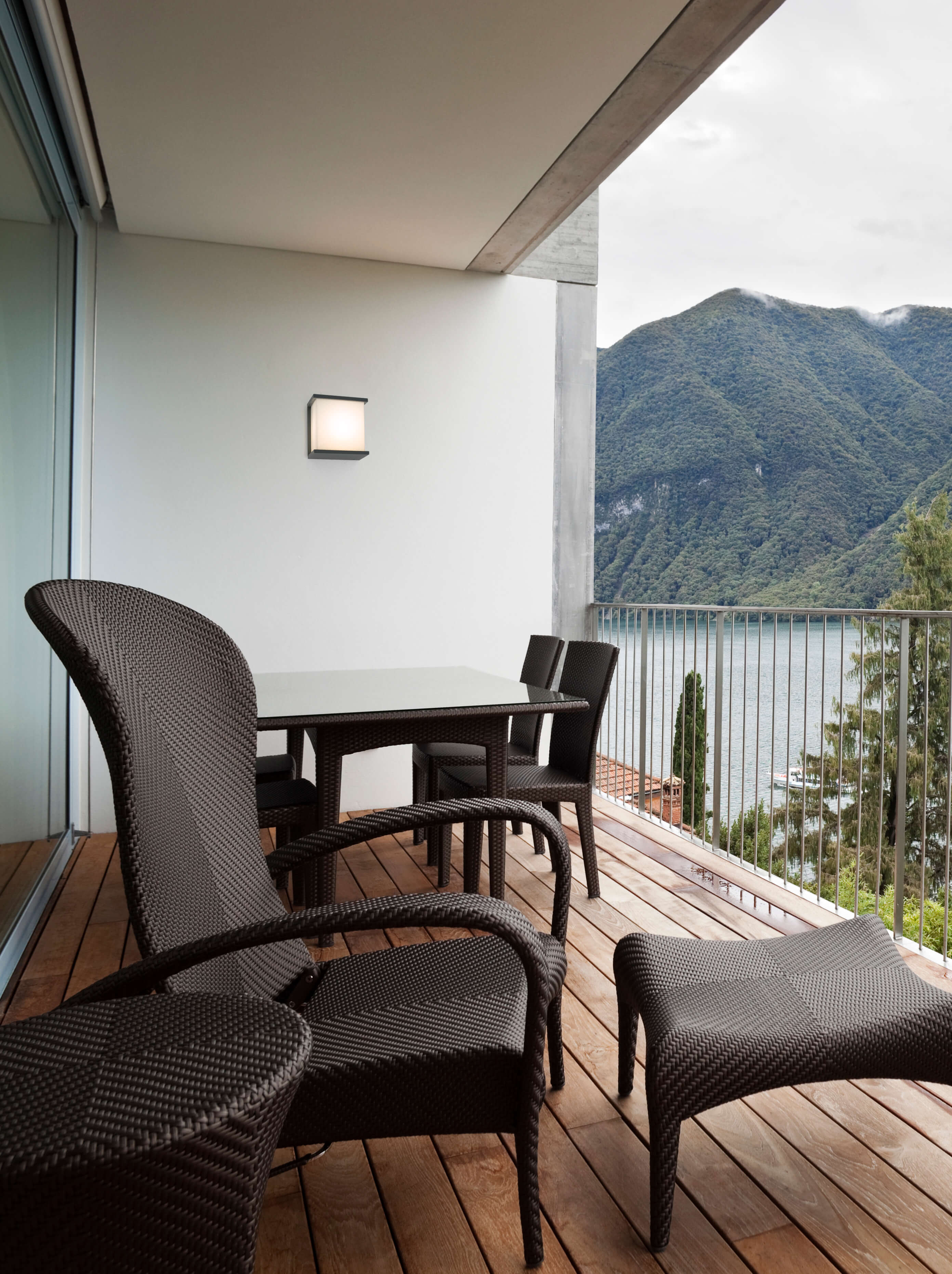 Balkon mit Terrassenmöbeln, einem See und Bergen im Hintergrund.