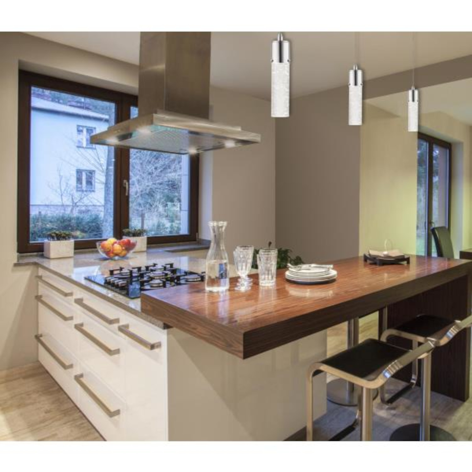 Una cucina moderna con mobili bianchi, un bancone in legno con sgabelli e lampade a sospensione.