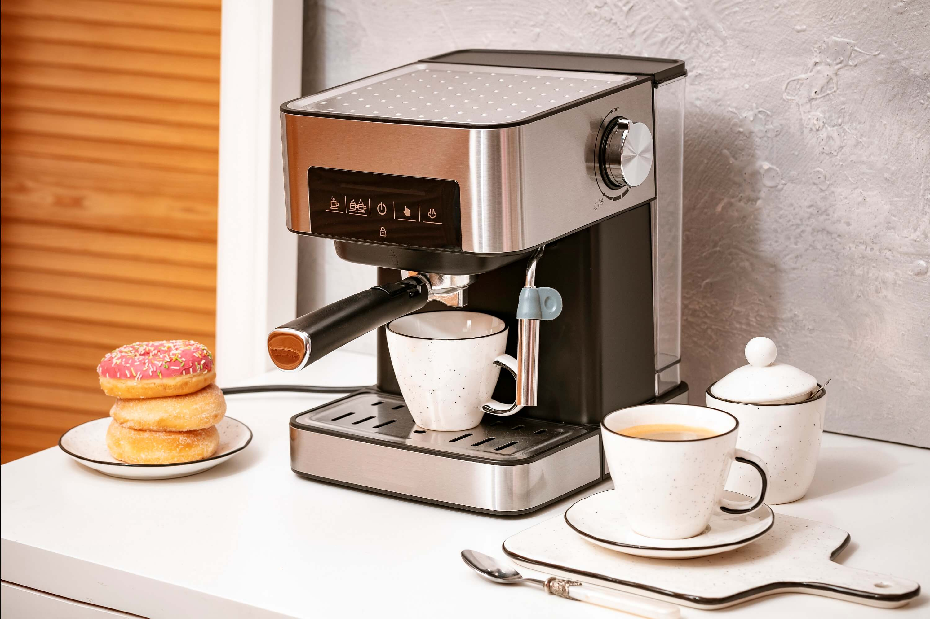 Srebrno-czarny ekspres do kawy z pączkami, filiżankami do kawy i cukiernicą na stole.