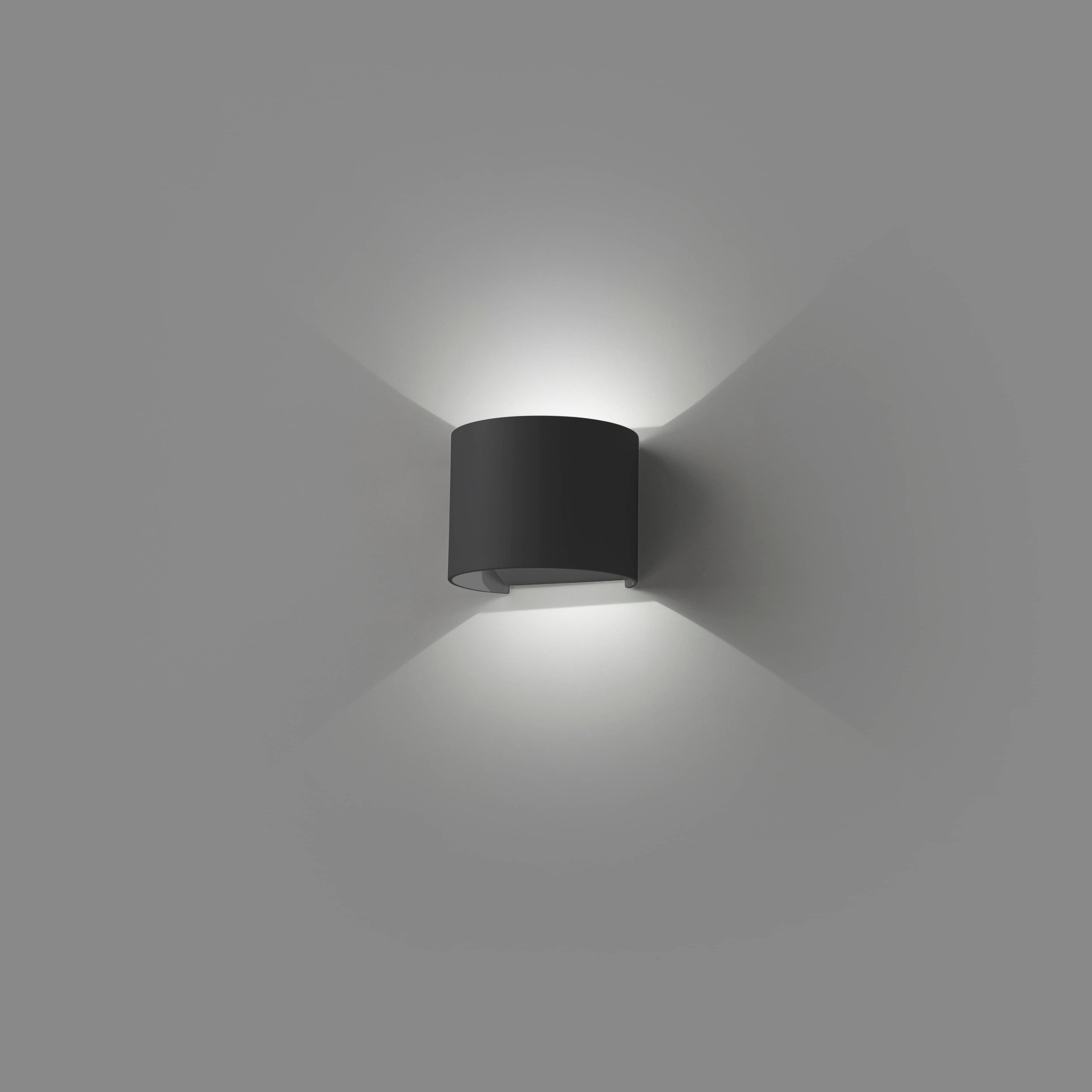 Eine schwarze Wandleuchte, die nach oben und unten Licht abgibt, an einer Wand montiert.