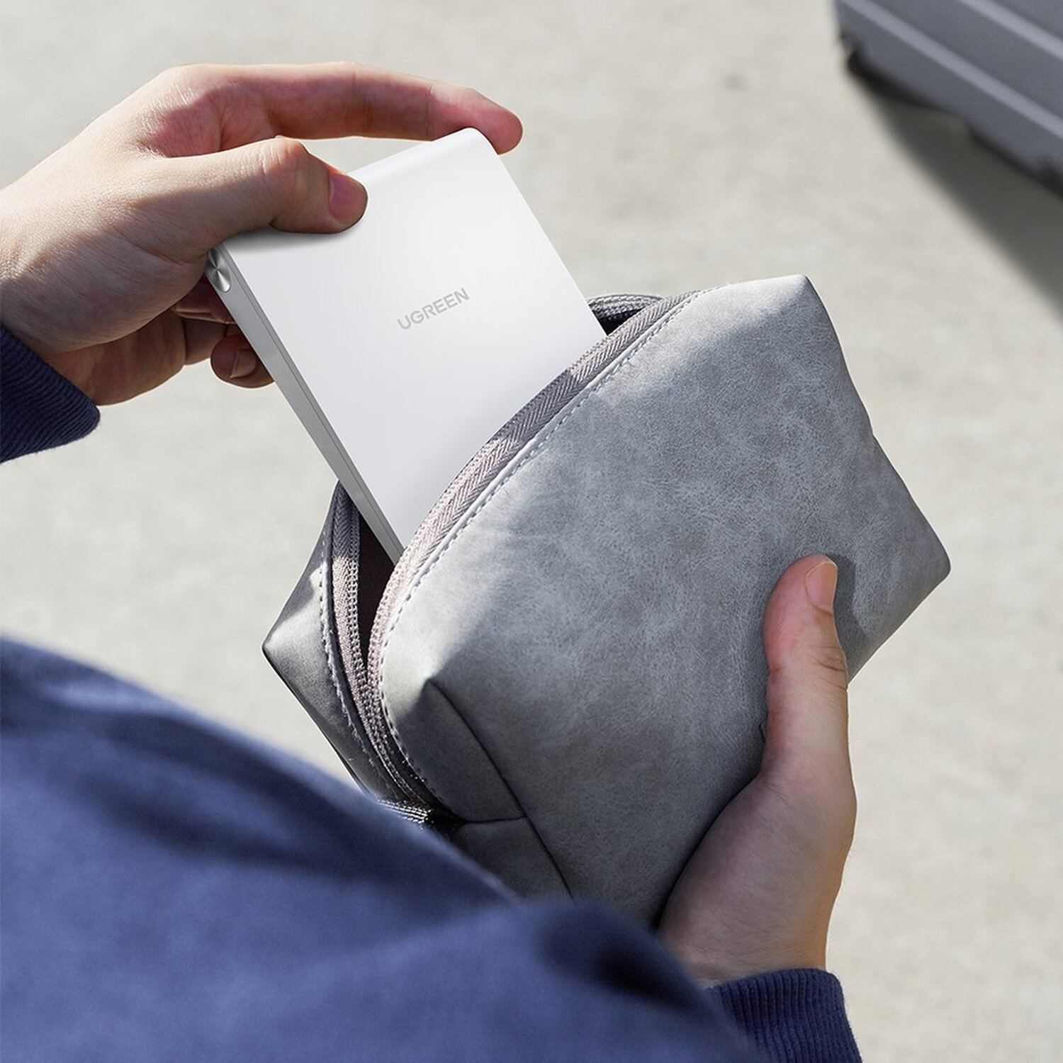 Hände halten ein weißes UGREEN-Gerät, das sich in einer grauen Tasche befindet.