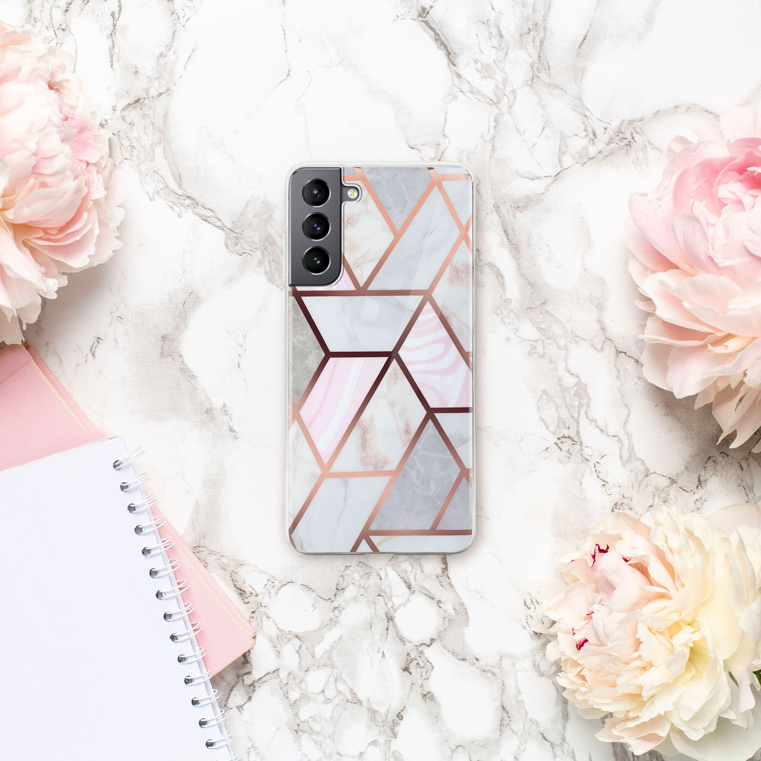 Telefon in einer marmorierten Hülle, mit rosa Blumen und einem Notizbuch.
