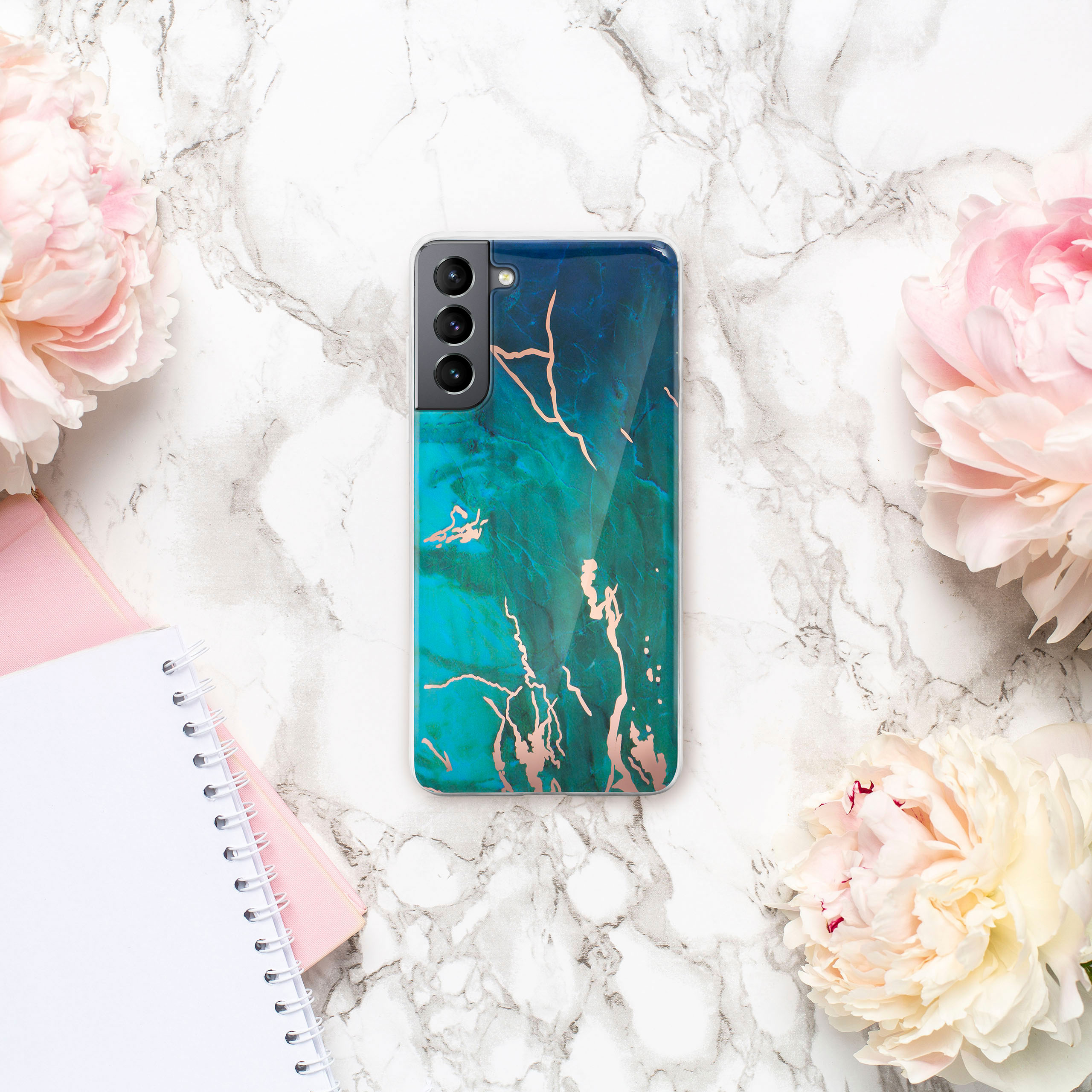 Smartphone in einer Hülle mit Marmor-Design, umgeben von Blumen und Schreibwaren.