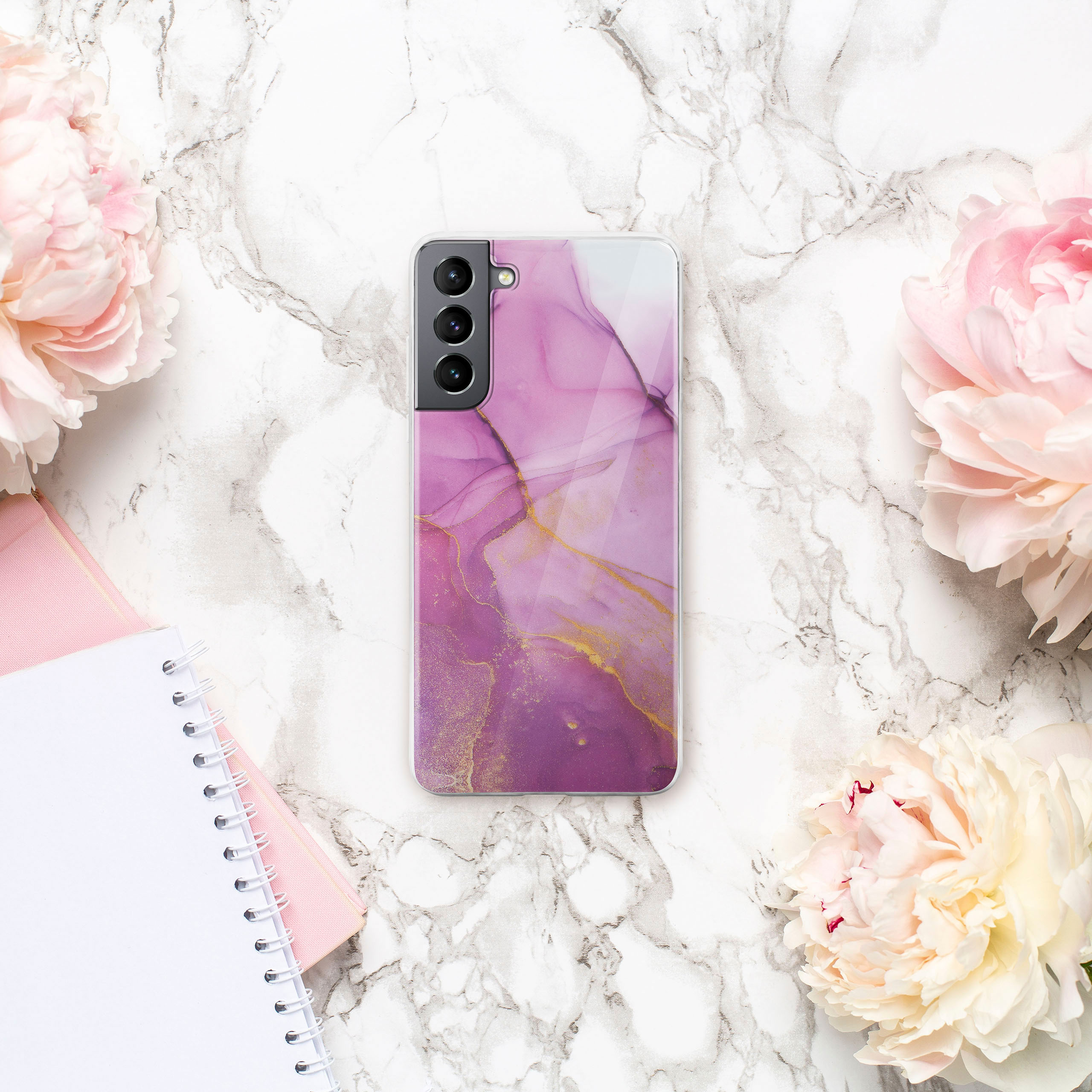 Telefon auf Marmorhintergrund mit rosa Blumen und Notizbuch.