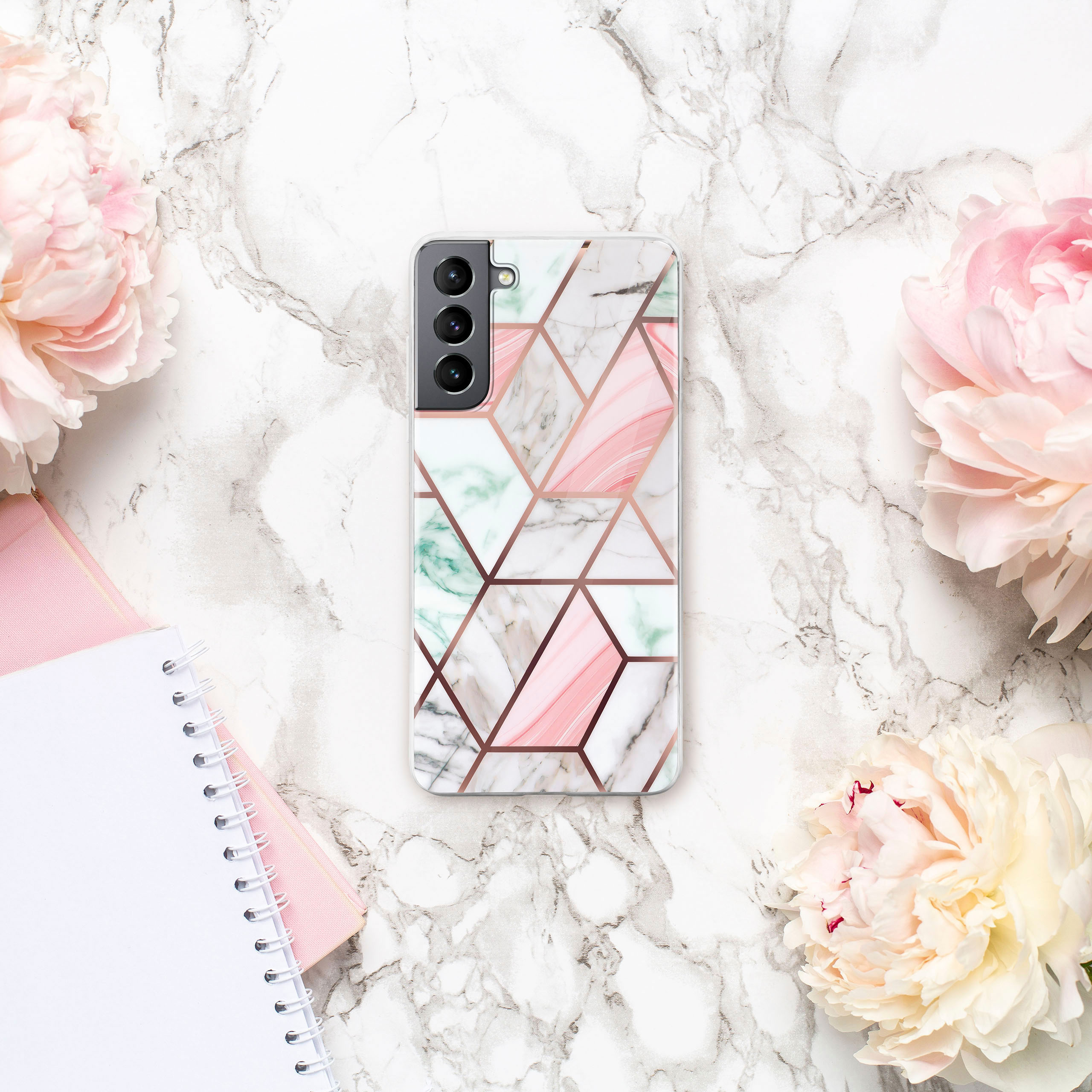 Ein Telefon mit Marmormuster liegt auf einer Marmoroberfläche mit rosa Blumen.