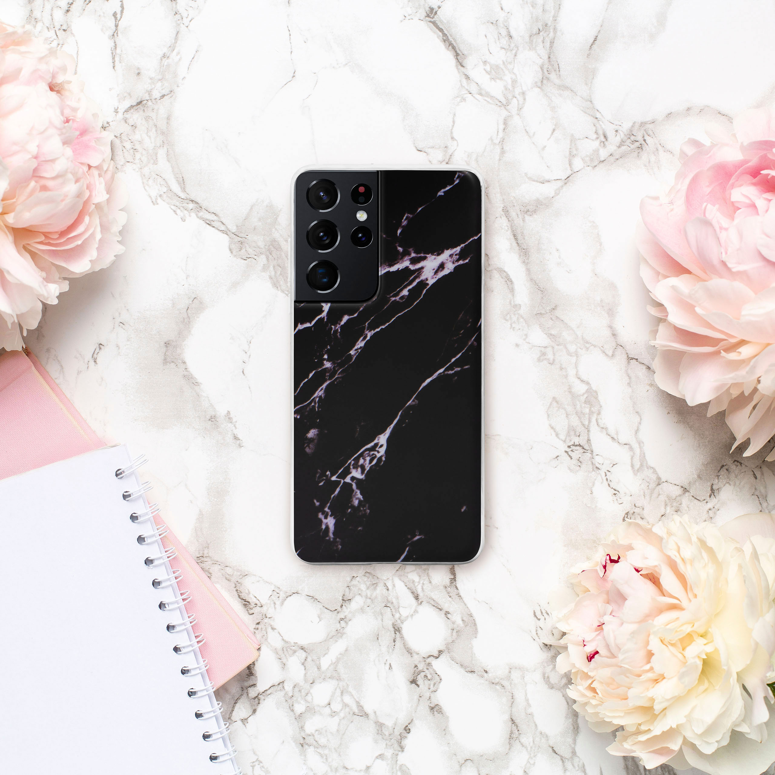 Telefon mit Marmorgehäuse auf Marmoroberfläche mit rosa Blumen und Notizbüchern.