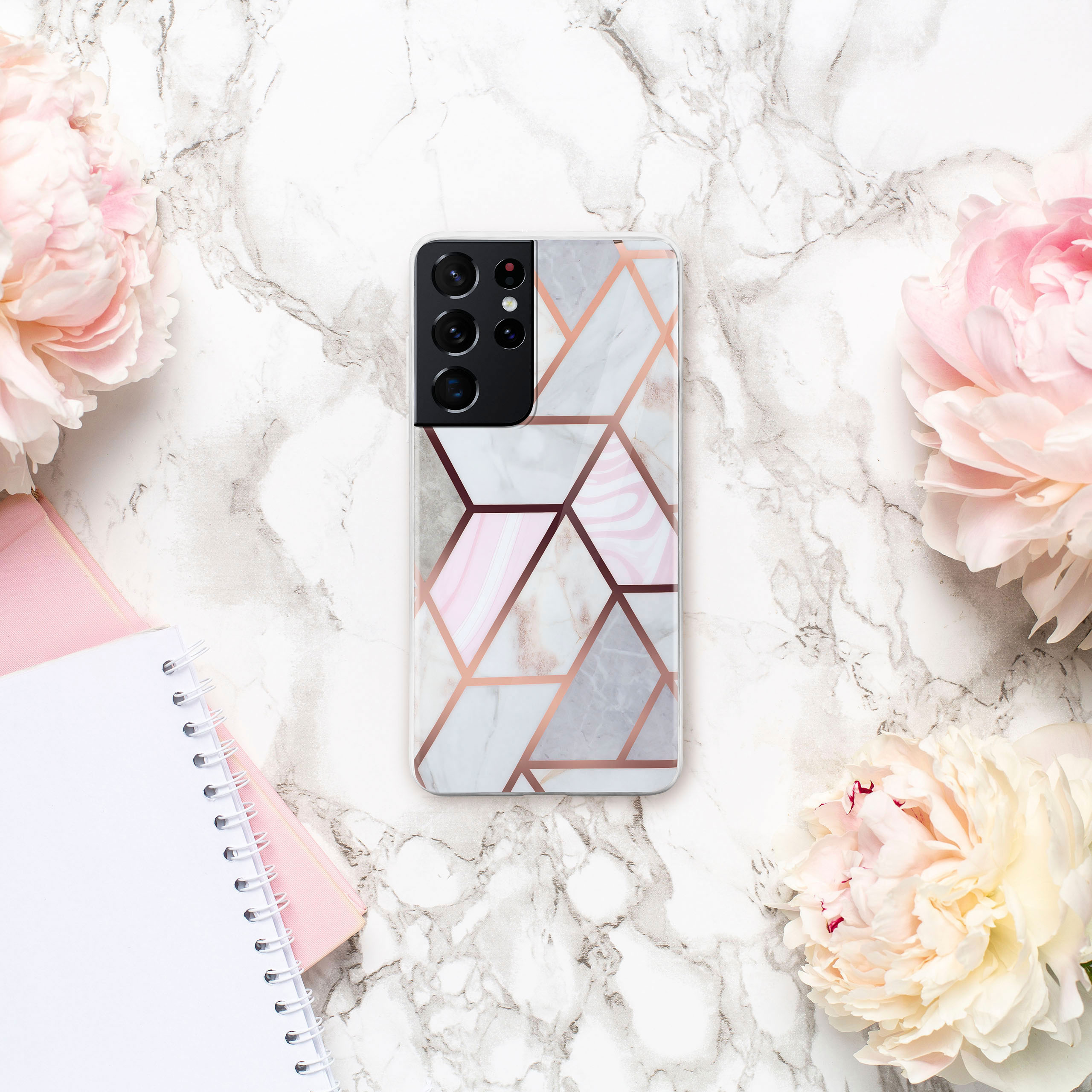 Handyhülle mit geometrischem Muster auf Marmoroberfläche mit rosa Blumen und Notizbüchern.