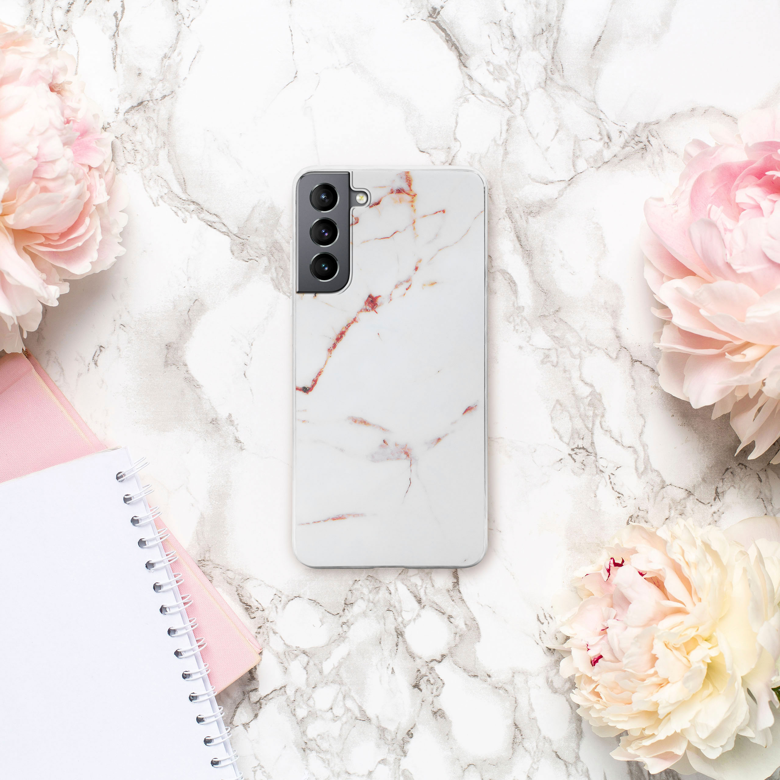 Marmor-Handyhülle mit Marmordesign, liegt zwischen Blumen und einem Notizbuch.