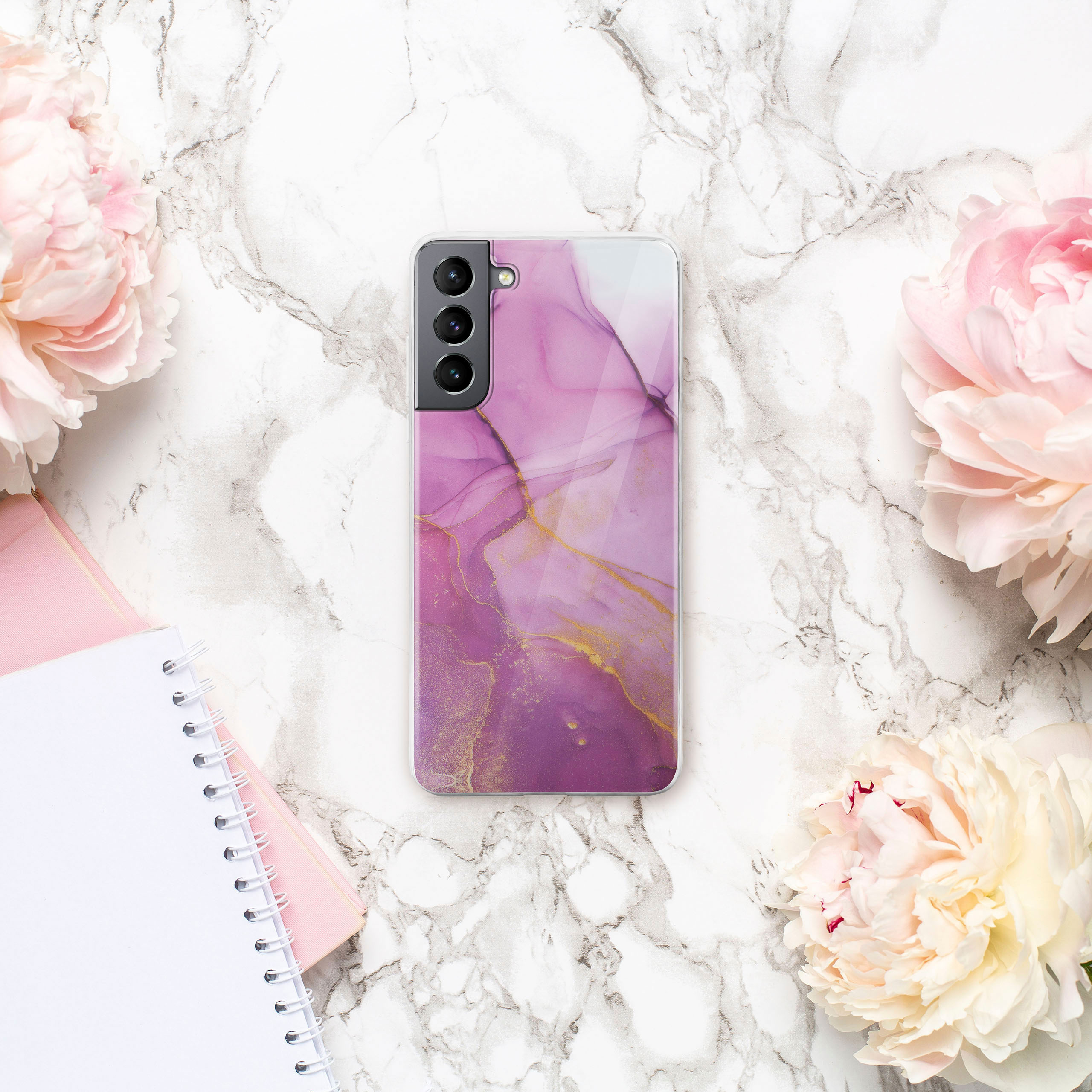 Eine Handyhülle mit rosa Marmordesign, platziert auf einer Marmoroberfläche mit Pfingstrosen und Notizbüchern.