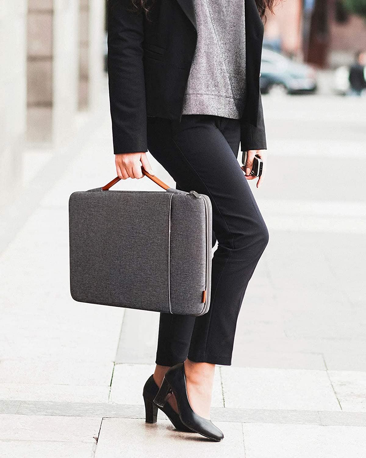 Una mujer con traje oscuro sostiene una bolsa gris para portátil con asa marrón.