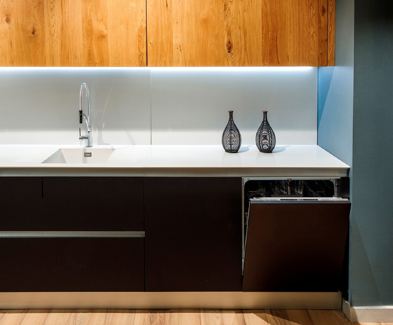Cocina moderna con armarios de madera, encimera blanca, fregadero y lavavajillas. Minimalista.