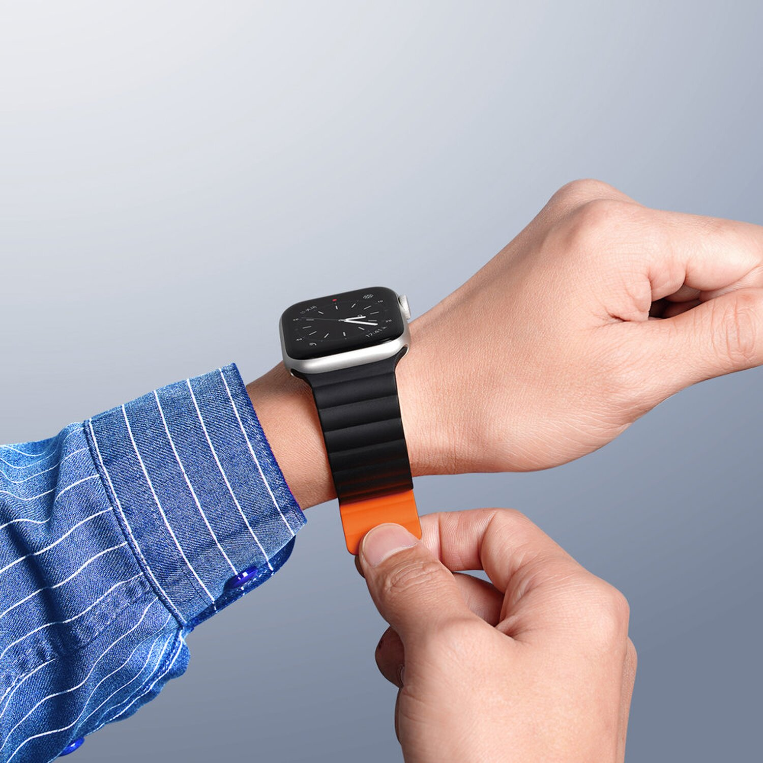 Hand stellt schwarzes und oranges Uhrenarmband am Handgelenk ein. Blauer Hemdärmel sichtbar.