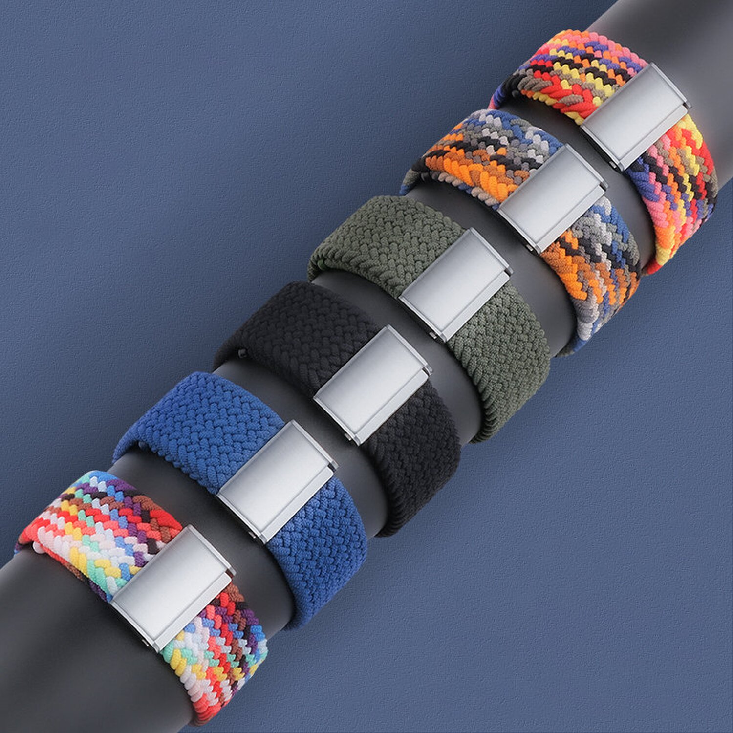 Mehrere geflochtene Uhrenarmbänder mit Metallverschlüssen, verschiedene Farben, auf blauem Hintergrund.