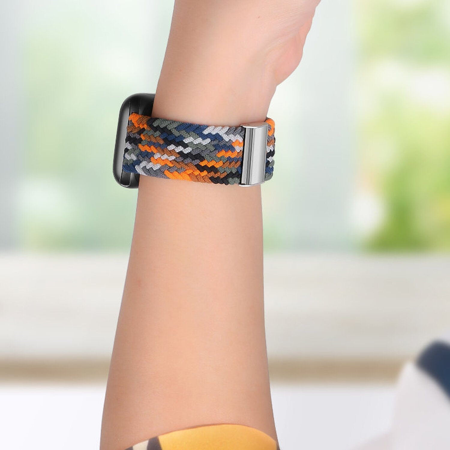Ein Handgelenk mit einer Uhr und einem bunten Uhrenarmband. Das Band ist blau, orange und grau. Der Hintergrund ist unscharf.
