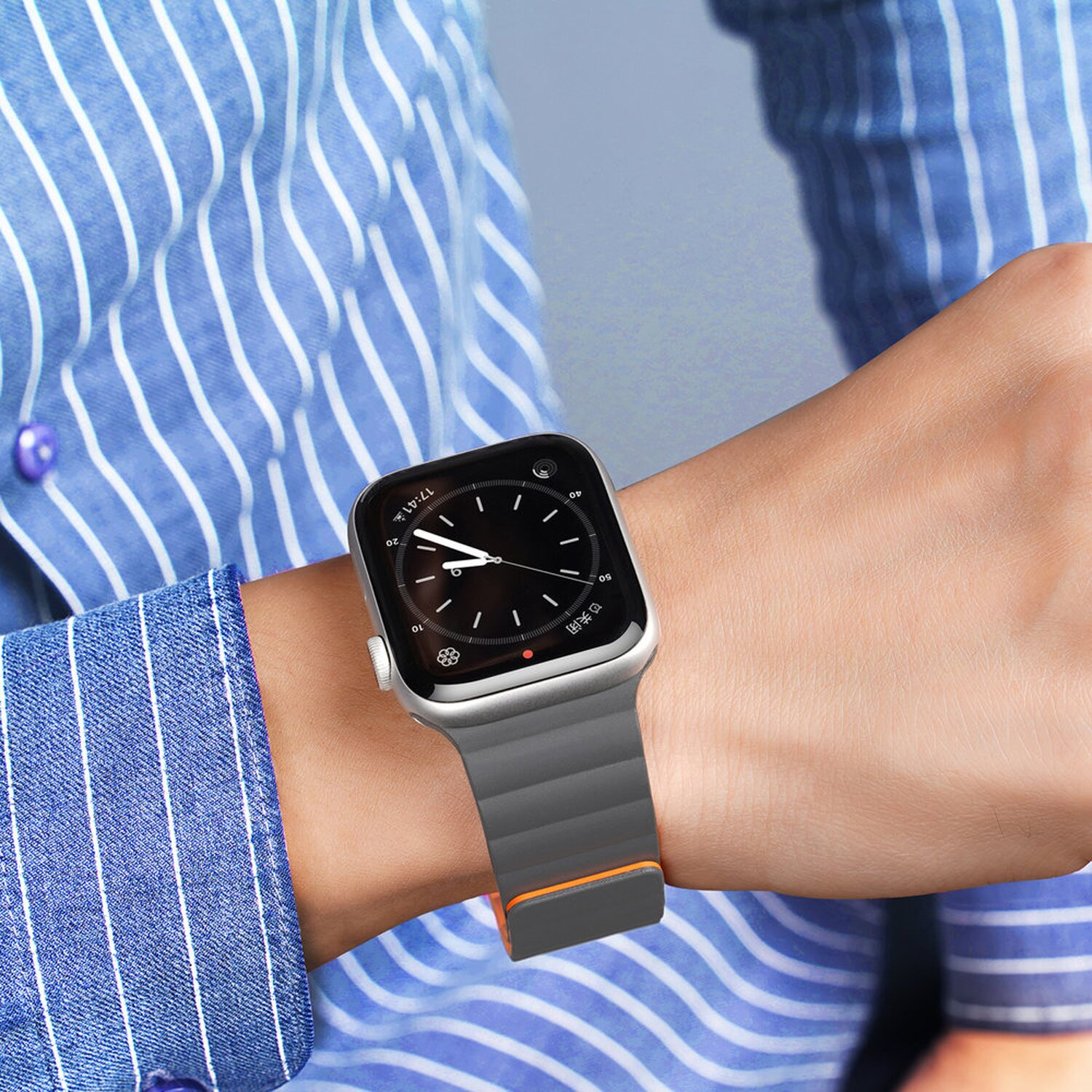 Person trägt eine Uhr mit grauem Armband, orangefarbenen Akzenten. Blaues Hemd mit Streifen.