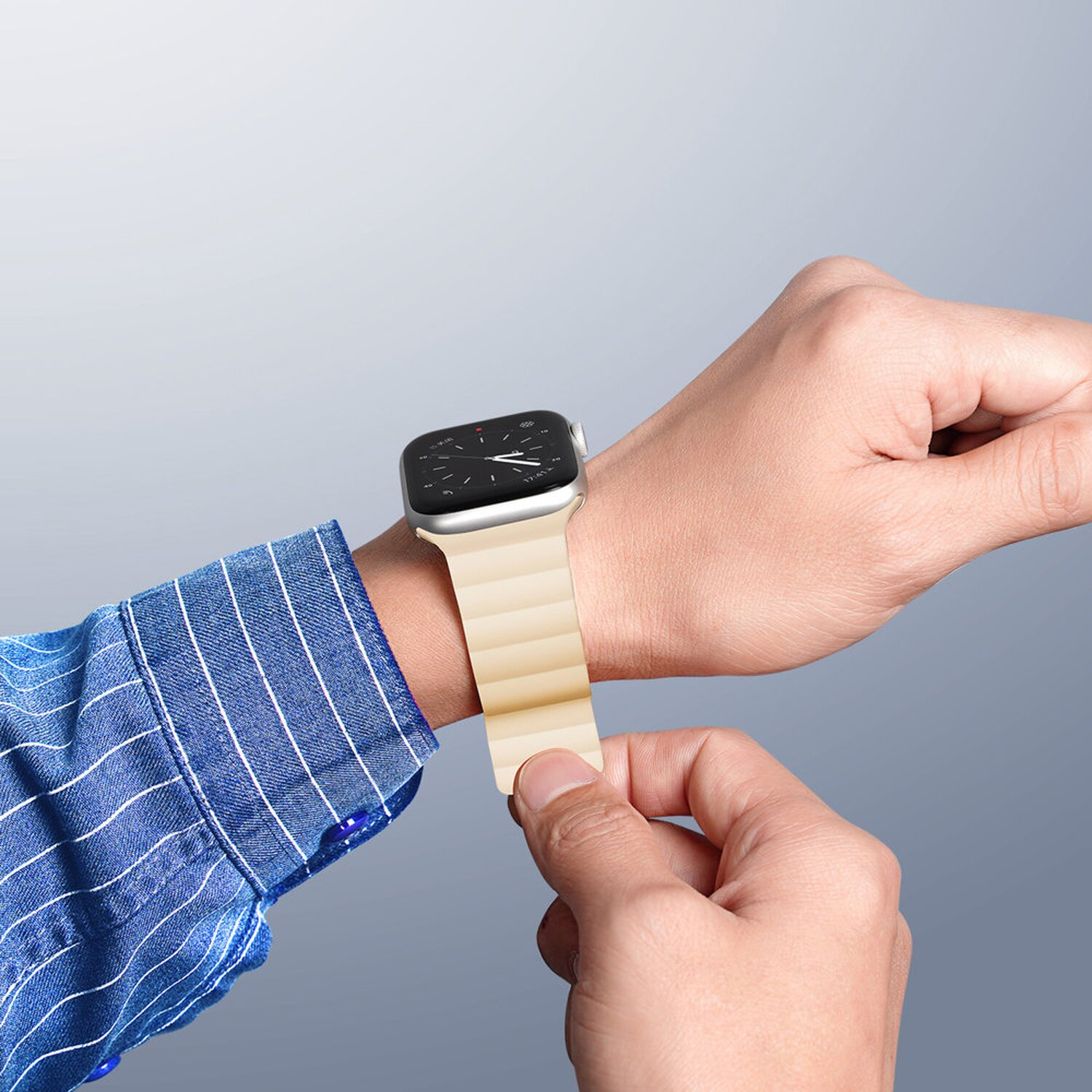 Person trägt ein cremefarbenes Armband an einer silbernen Apple Watch. Blaues Hemd.